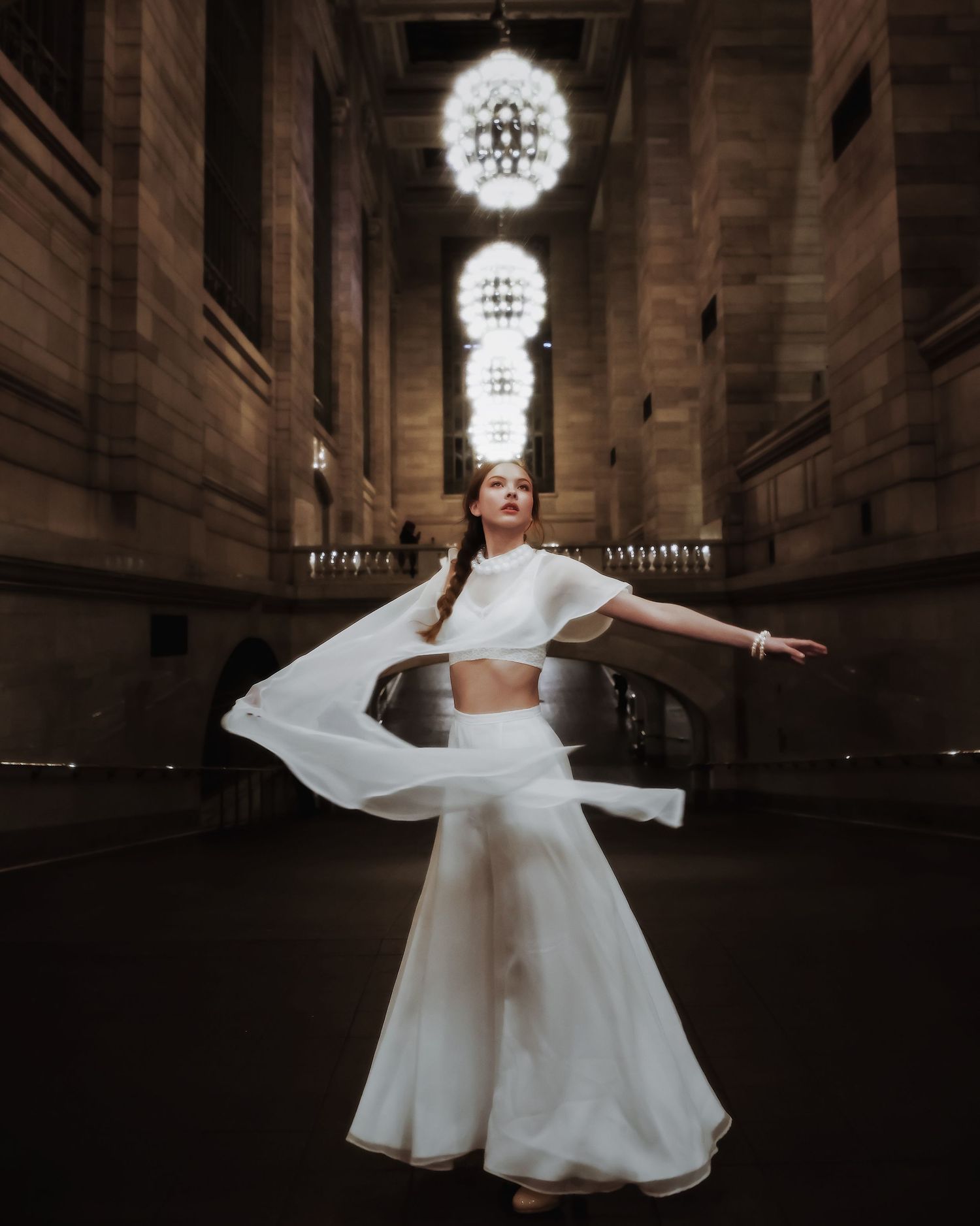 A bride in a flowing white dress twirls gracefully inside a grand historic building with ornate chandeliers.