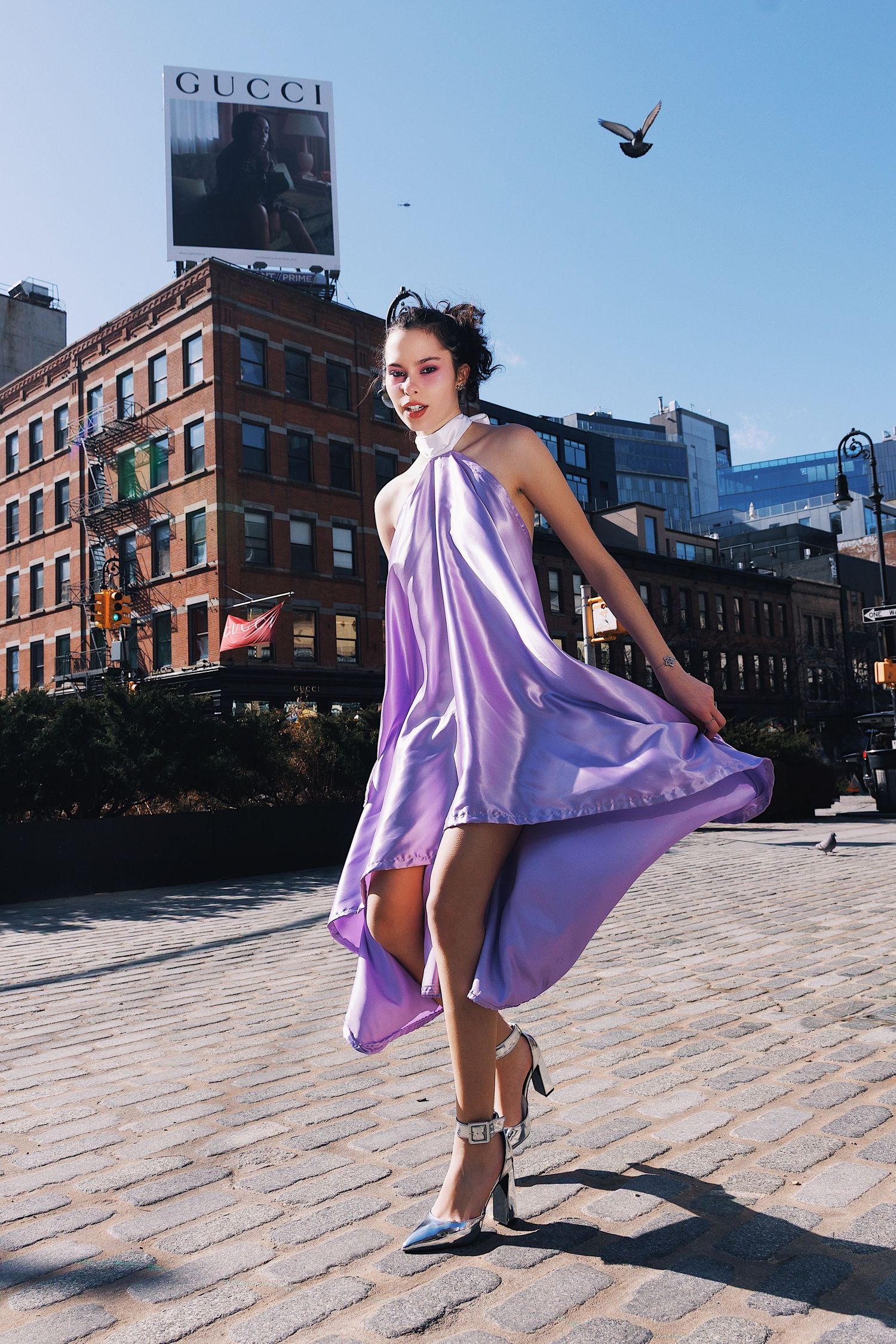 A dancer in a flowing purple dress twirls gracefully in an urban setting with brick buildings and cobblestone streets.