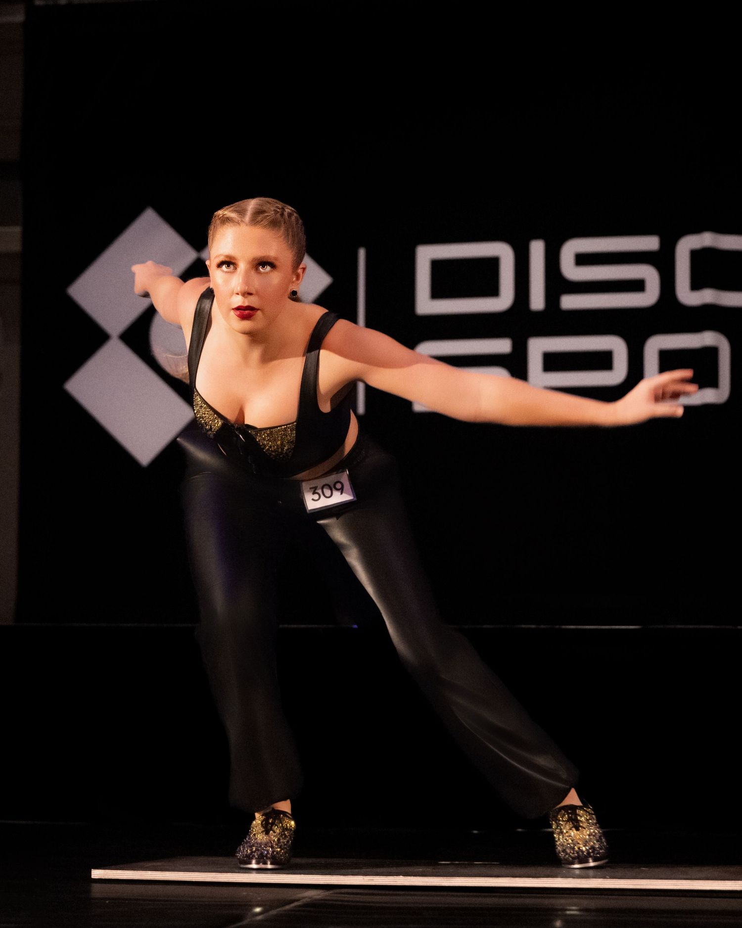 A dancer in black attire performs an energetic pose on stage during a dance competition.