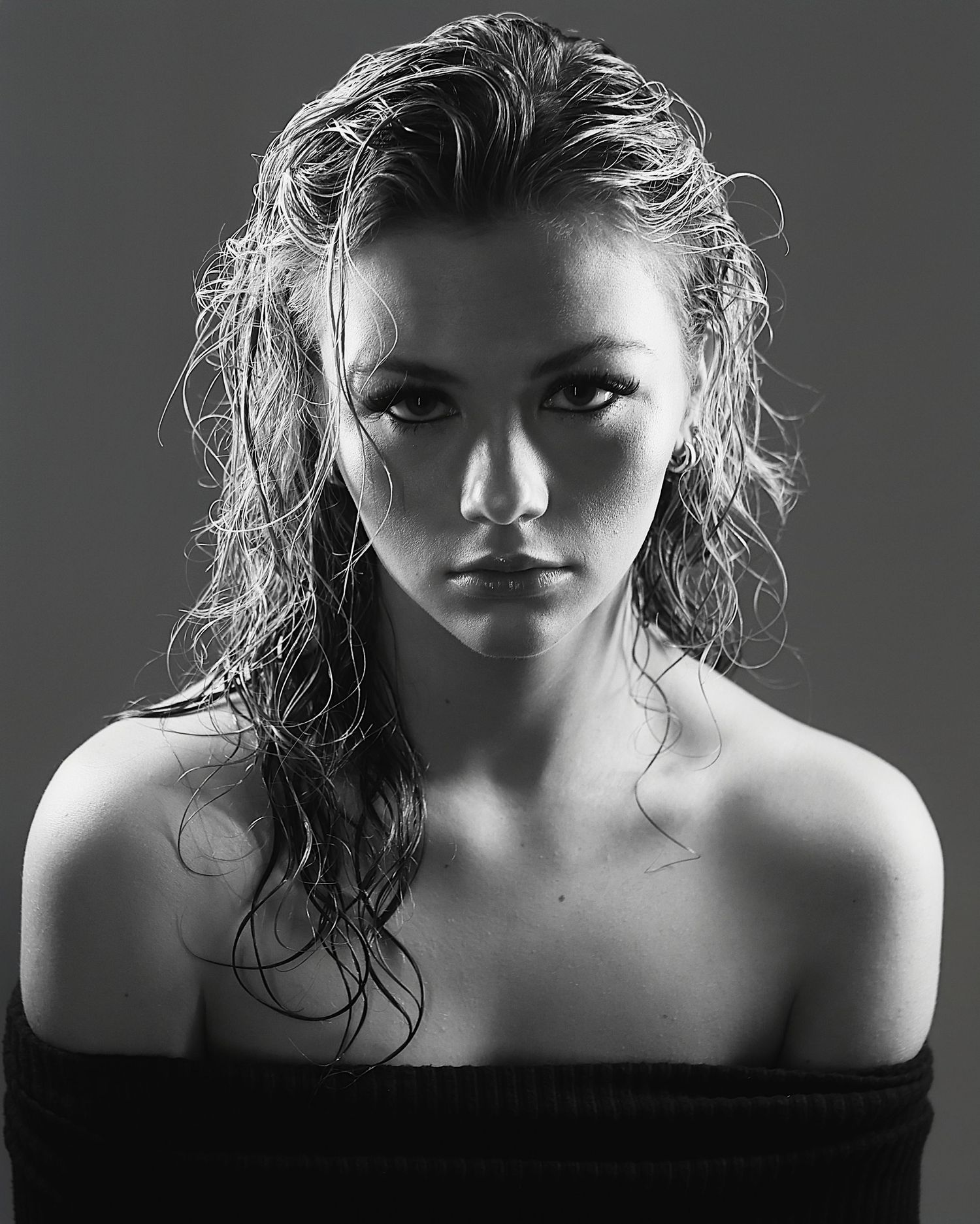 Dramatic black and white portrait with moody lighting shows figure with wet tousled hair and bare shoulders against dark background.