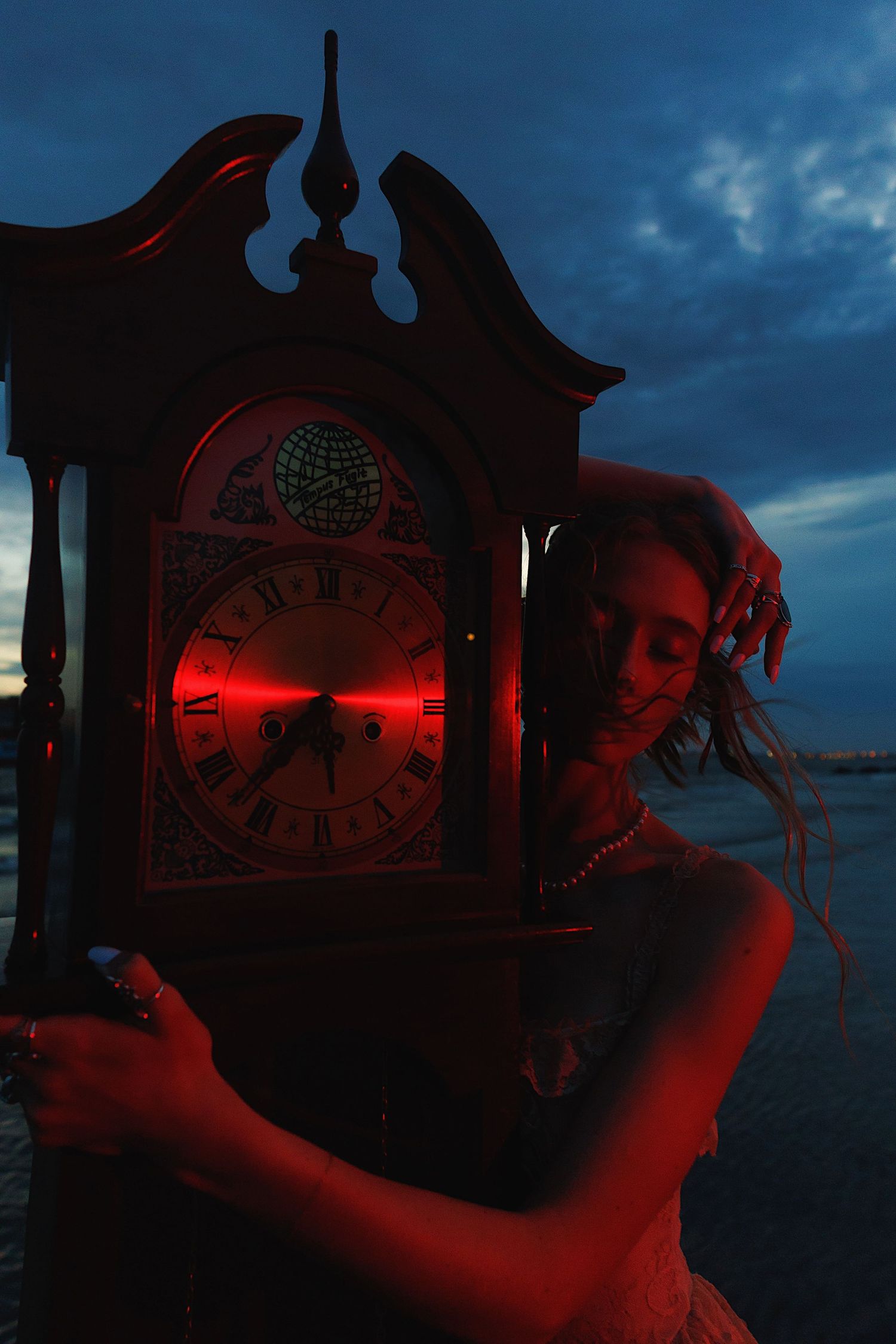 Red-illuminated antique clock faces glow against a dark blue twilight sky creating an eerie atmosphere.