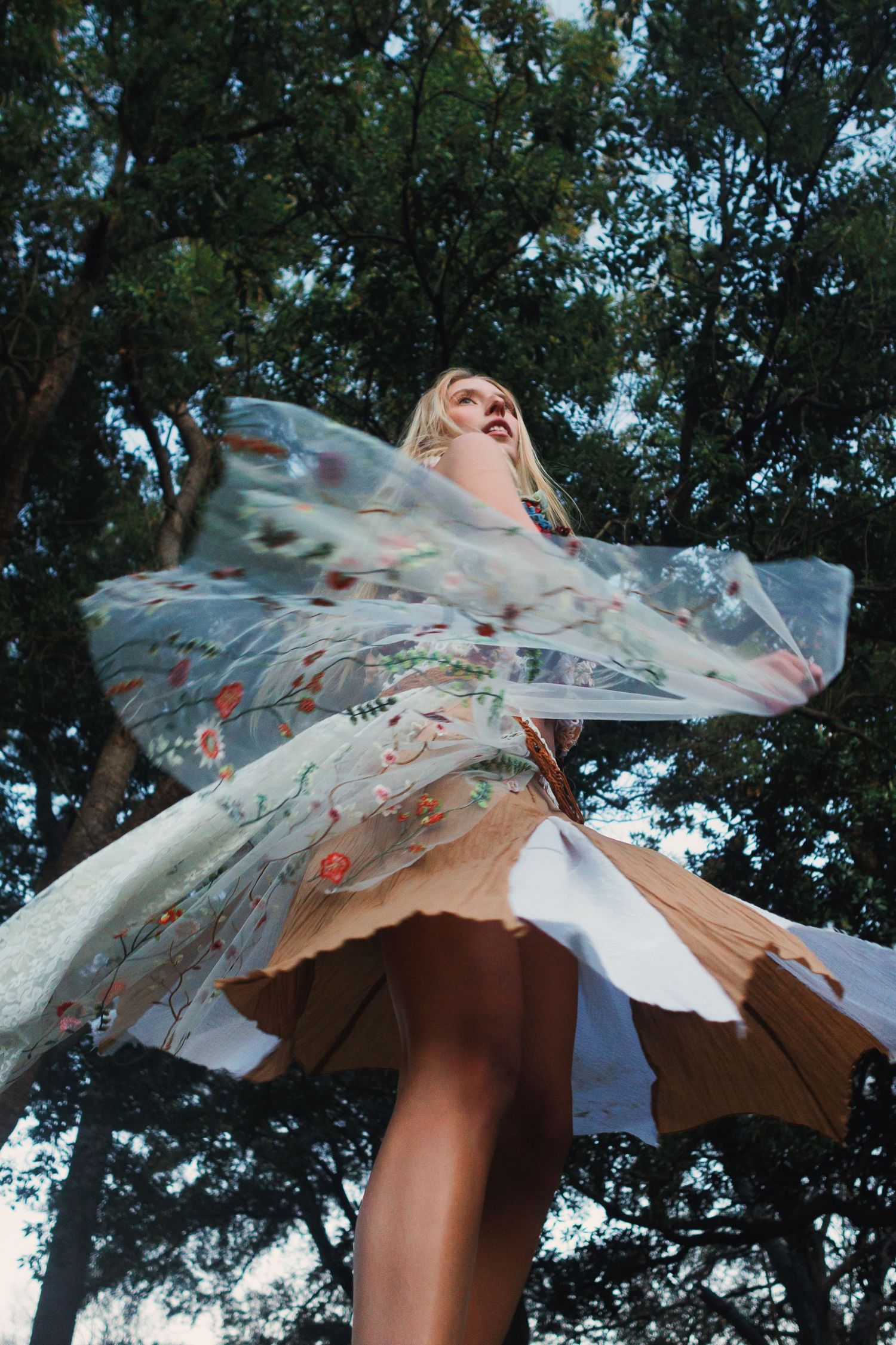 A white floral parasol spins gracefully against a backdrop of green trees, creating a dreamy summer scene.