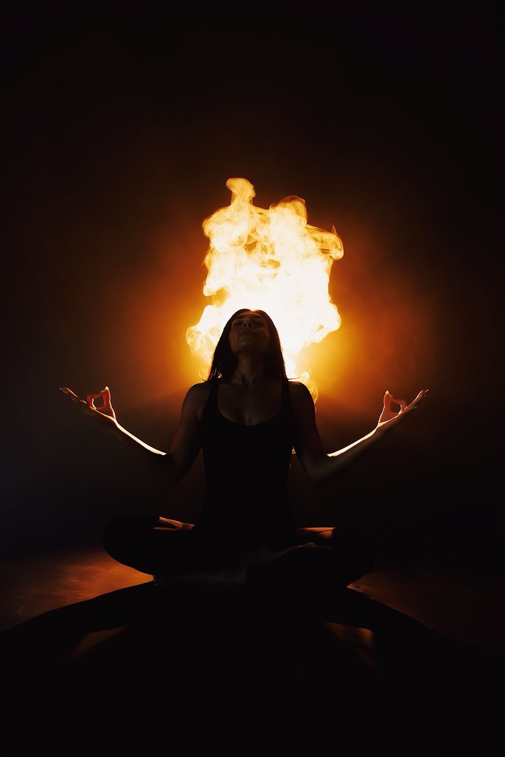 Silhouetted figure sits cross-legged against dark background with dramatic fire effects creating an ethereal atmosphere.