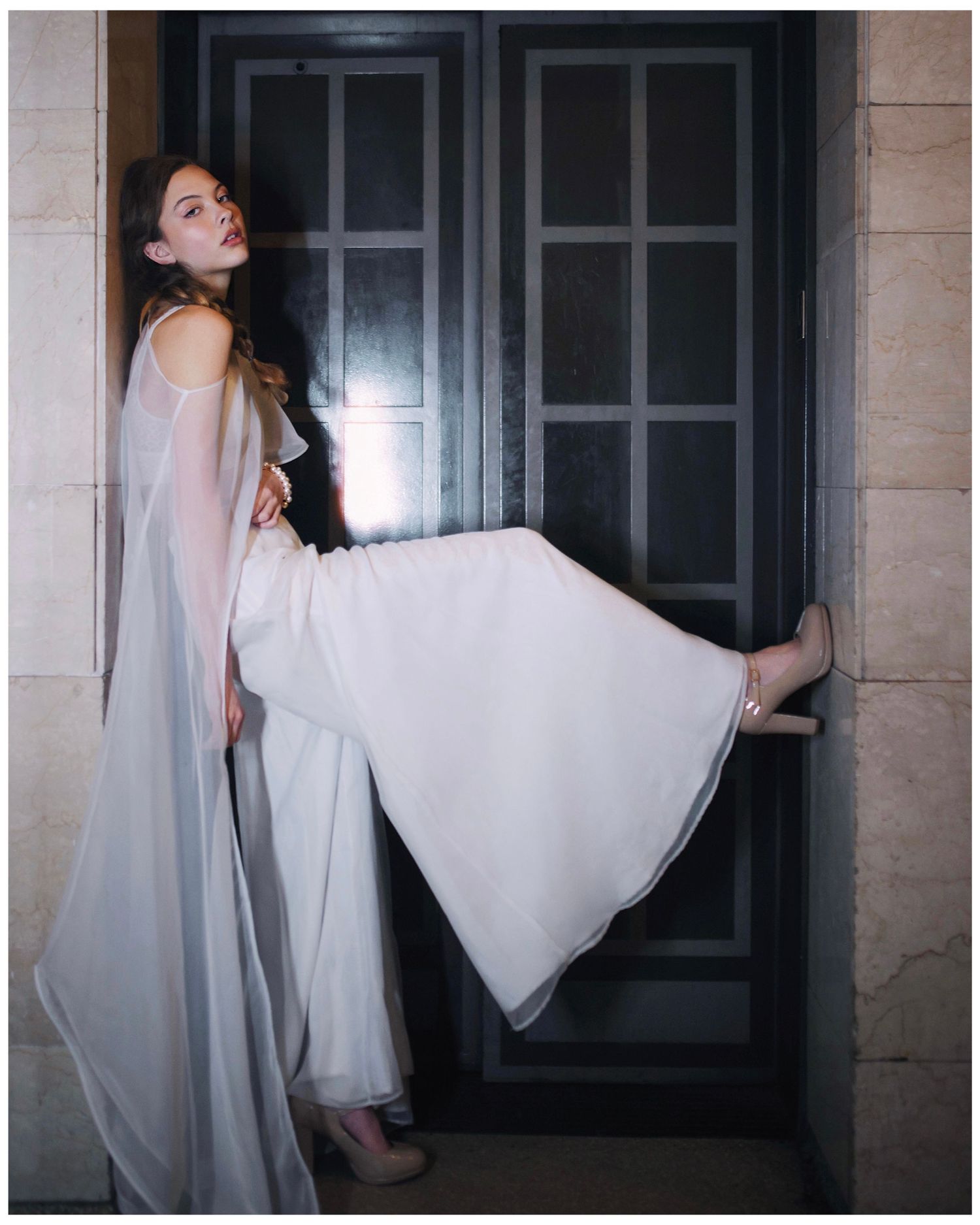 A figure in a flowing white dress moves dramatically against a dark doorway in an artistic photoshoot.
