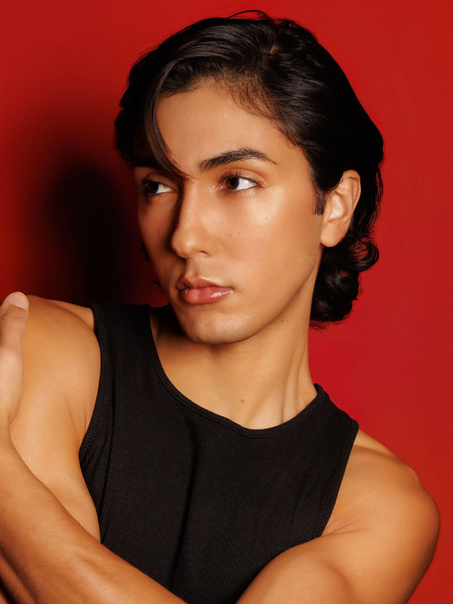 Portrait in a black sleeveless top against a red background with dramatic lighting and moody expression.