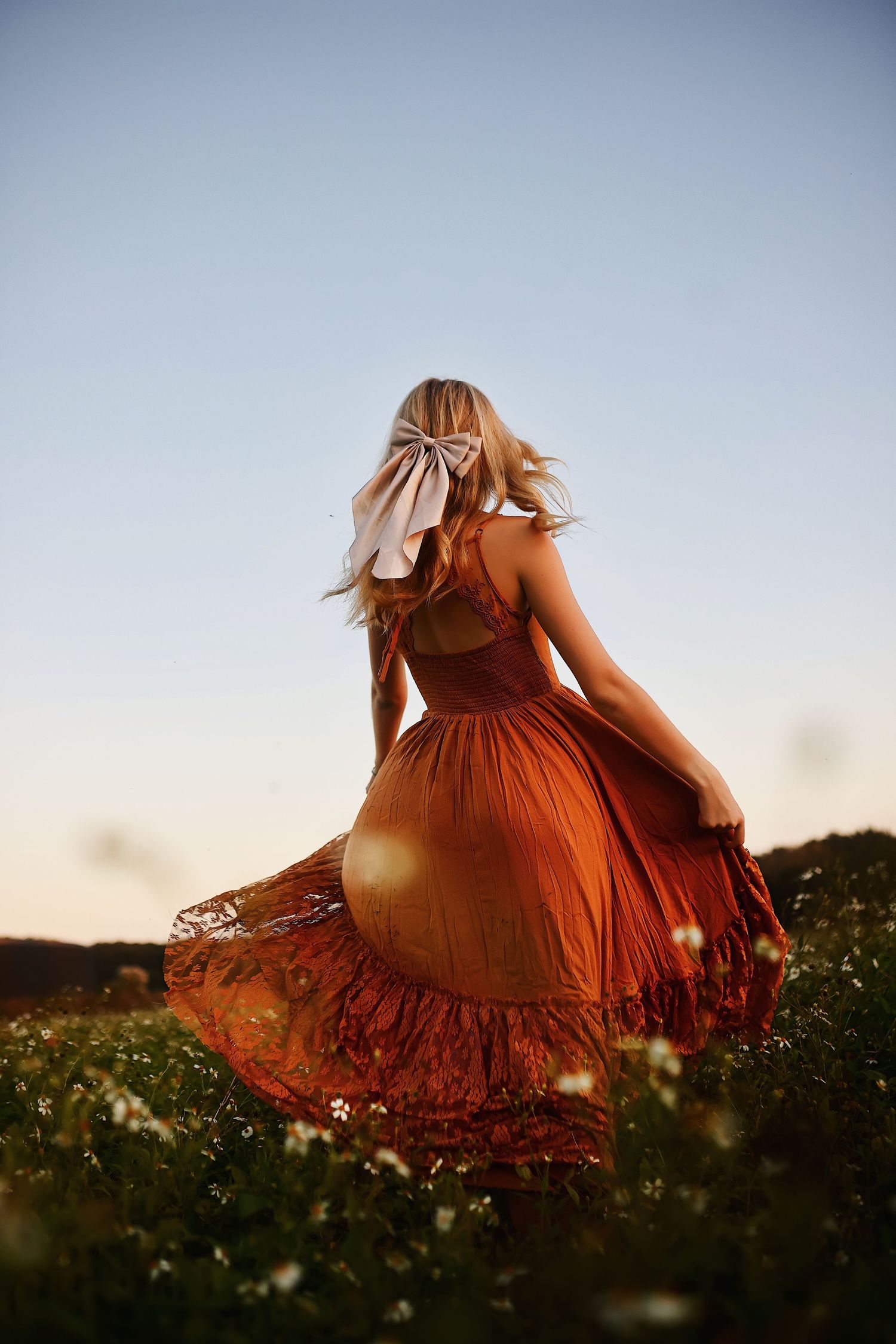 A person in a flowing rust-colored dress twirls through a wildflower meadow at sunset creating a dreamy silhouette.