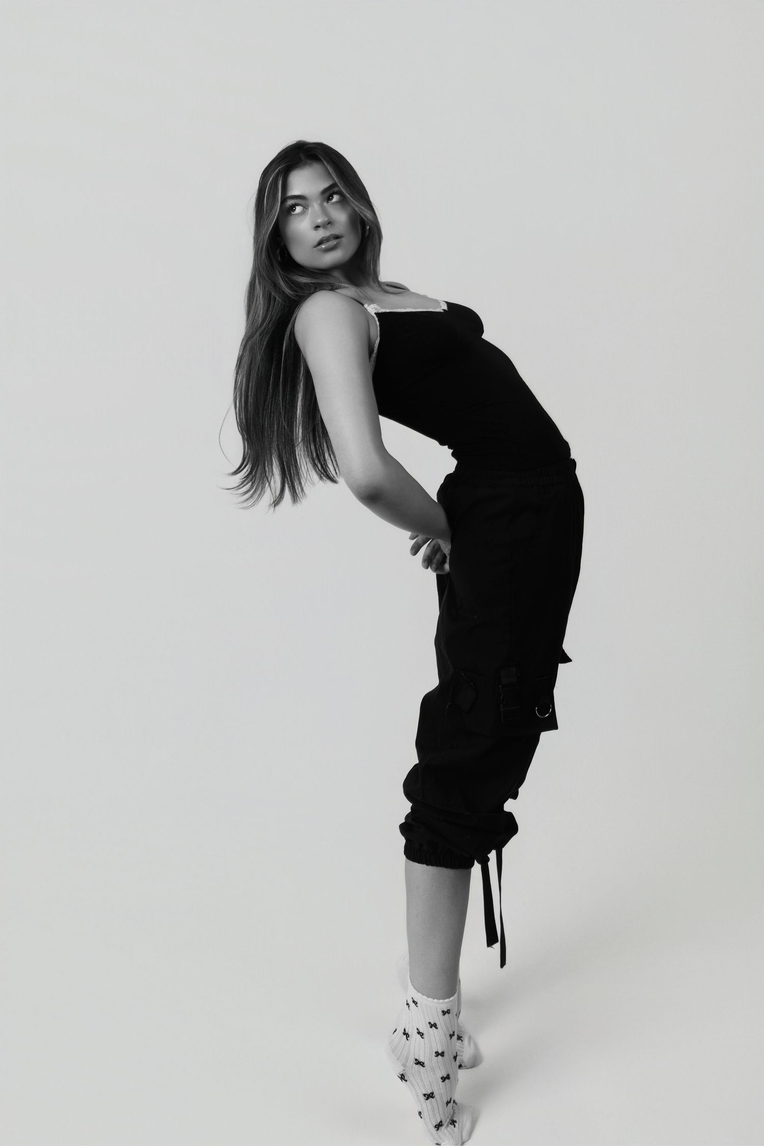 Fashion model poses in black dress and patterned boots against white background in artistic black and white portrait.