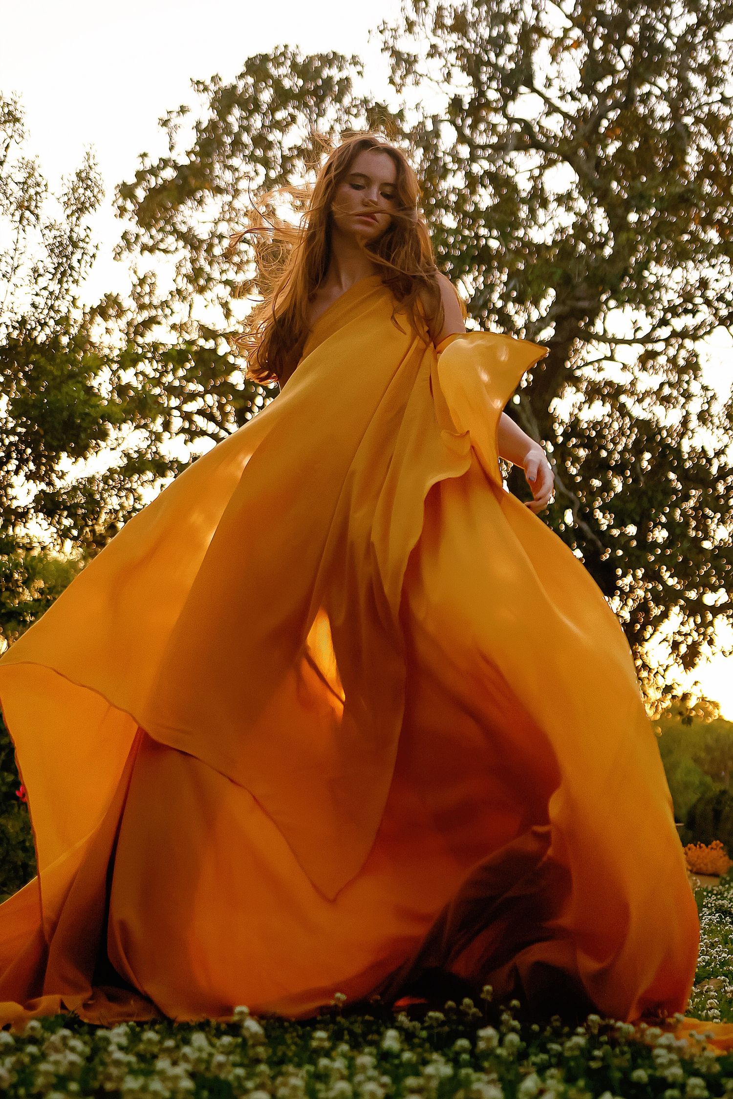 A flowy marigold yellow dress billows dramatically in an outdoor setting during golden hour.