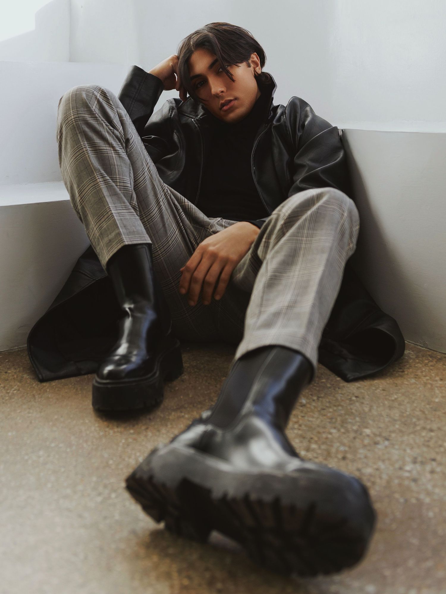 Fashion photo showcasing black combat boots and wide-leg trousers styled with a dark leather jacket in moody lighting.