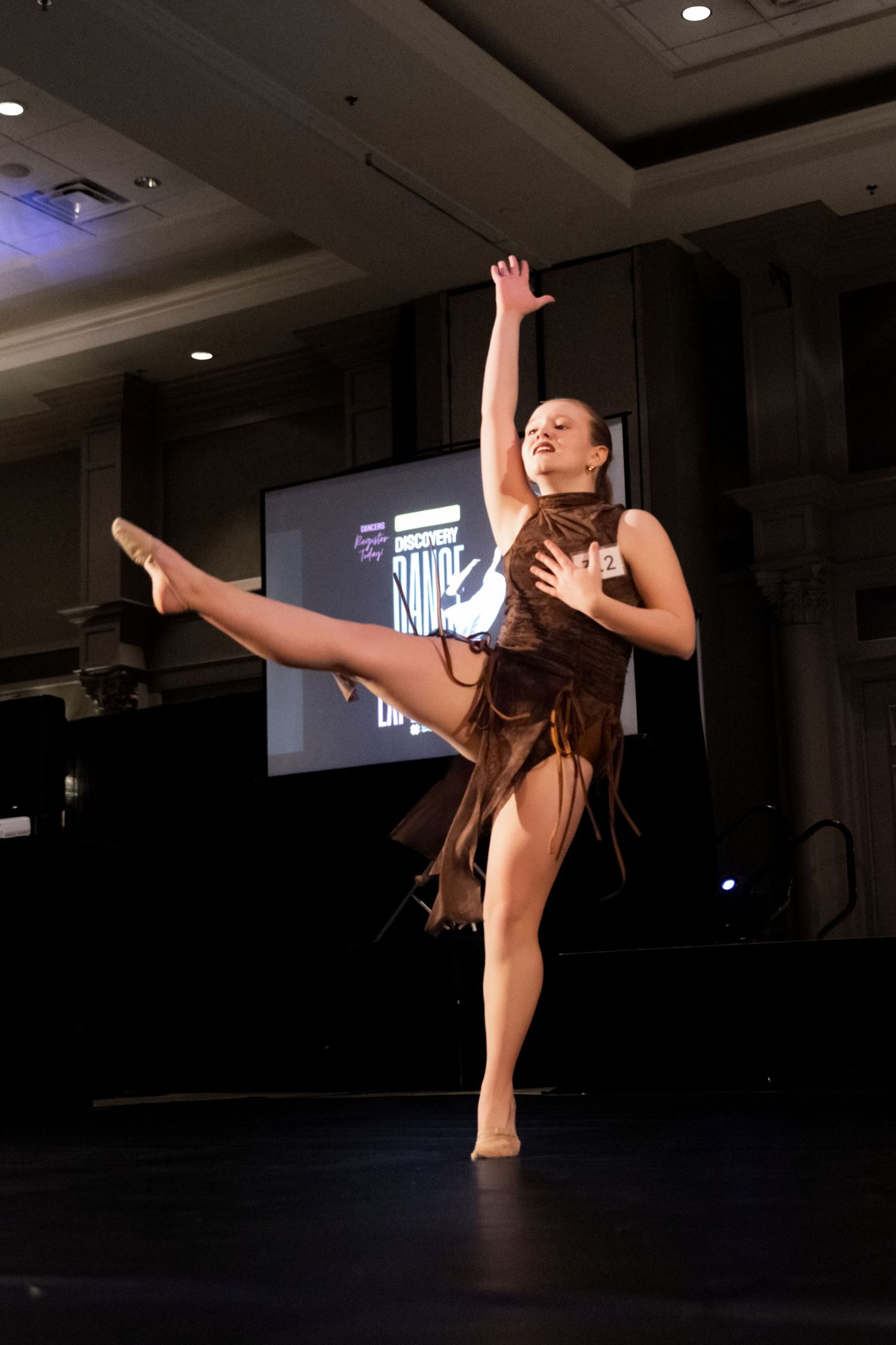 A dancer in black performs a dramatic high kick sequence on a dark stage with dramatic lighting.