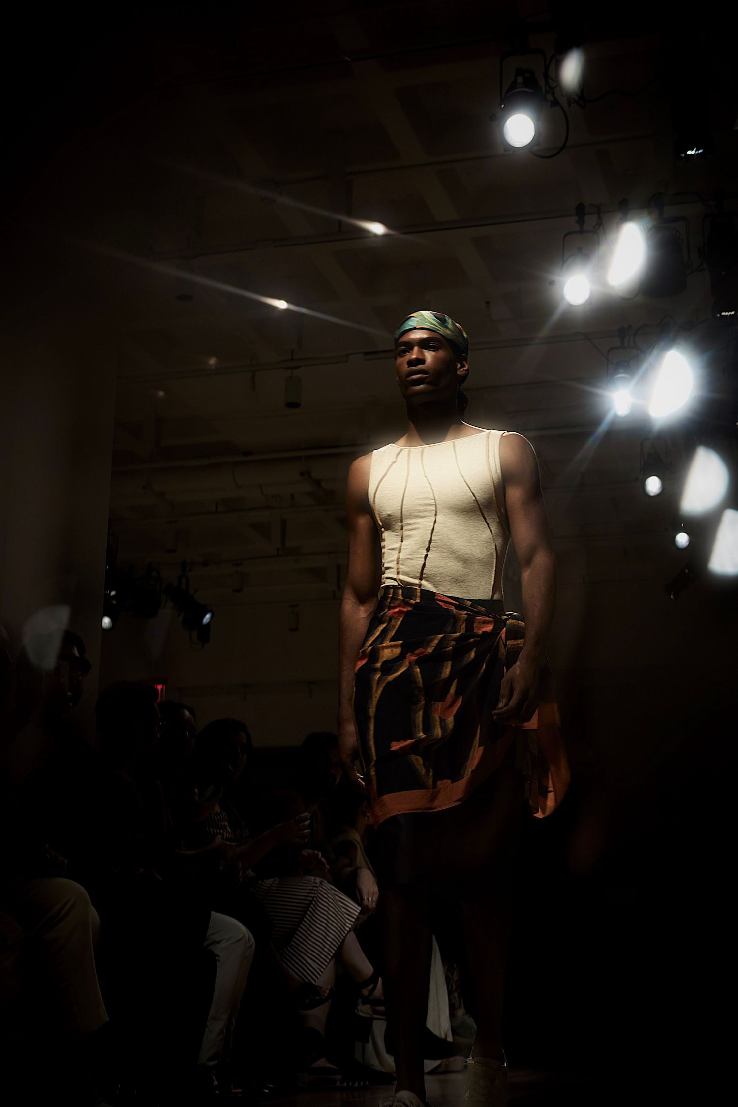 Models walk the runway in dark atmospheric lighting during a dramatic fashion show presentation.