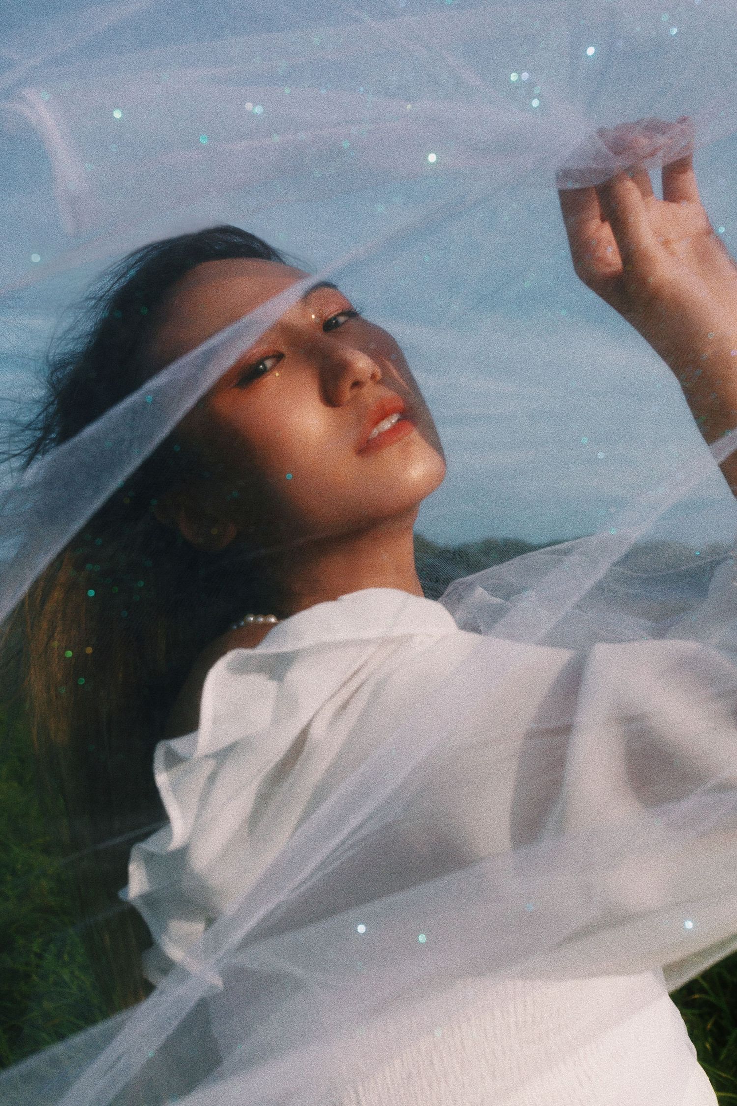 Ethereal portrait through sheer white fabric with sunlight creating a dreamy, romantic atmosphere outdoors.
