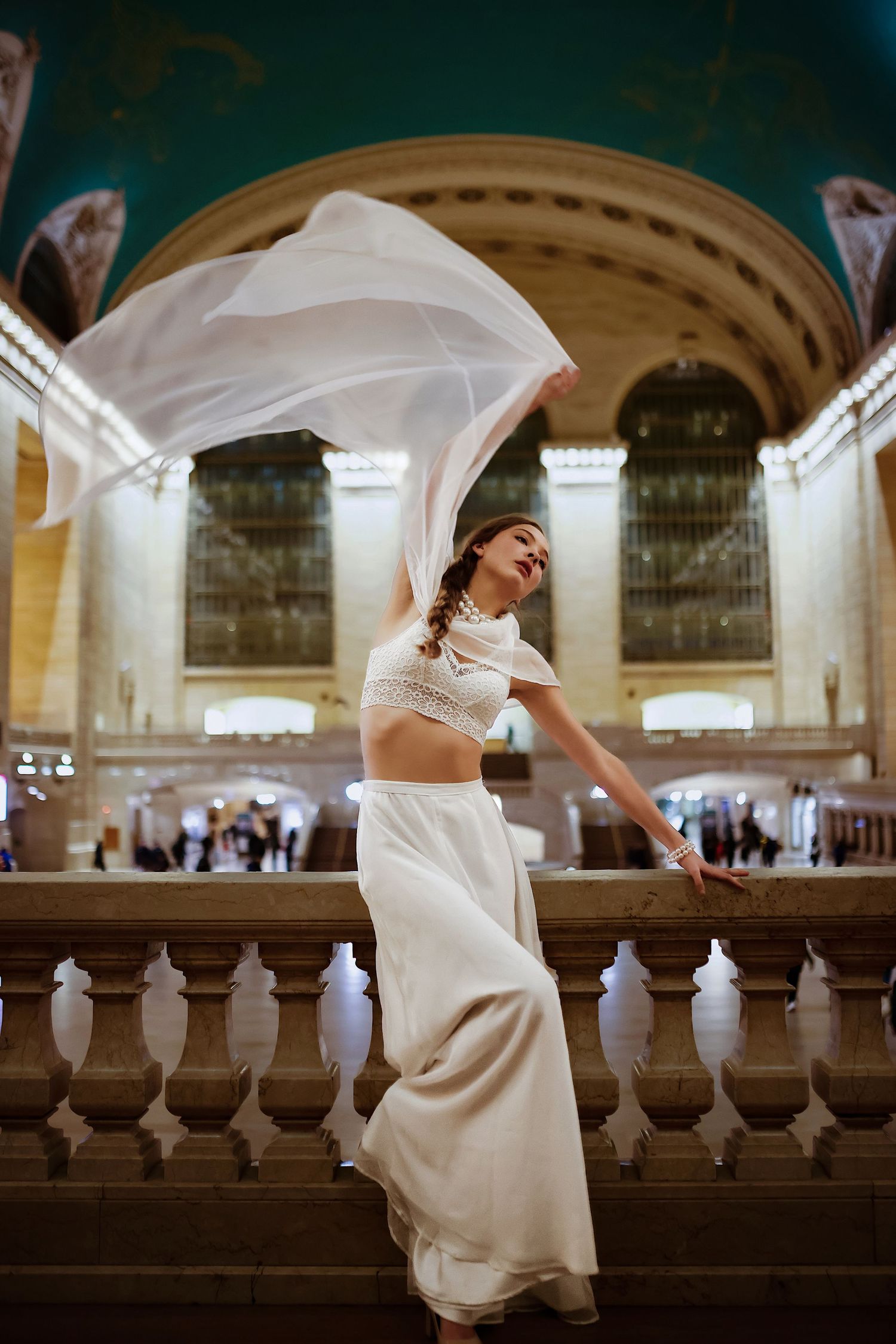 A dancer in a flowing white two-piece outfit performs gracefully on the grand staircase of Grand Central Terminal.