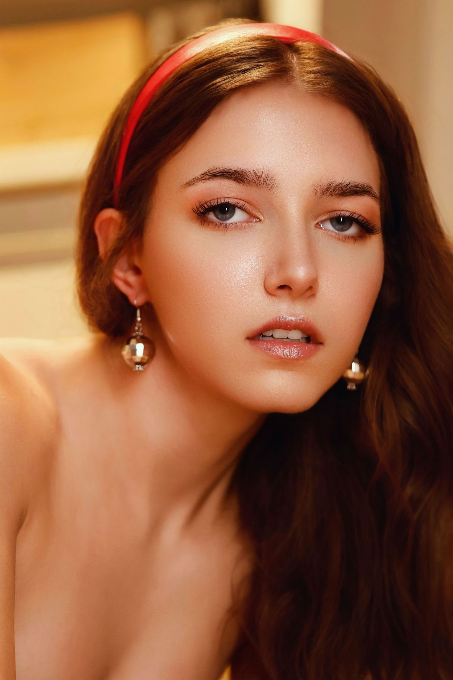 Portrait of a young woman wearing a red headband and crystal drop earrings in warm lighting.