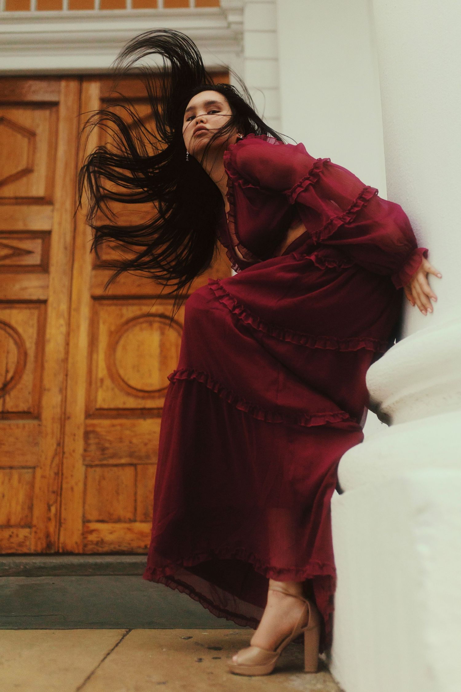 A dancer in a flowing burgundy dress twirls dynamically against a backdrop of wooden doors and white walls.