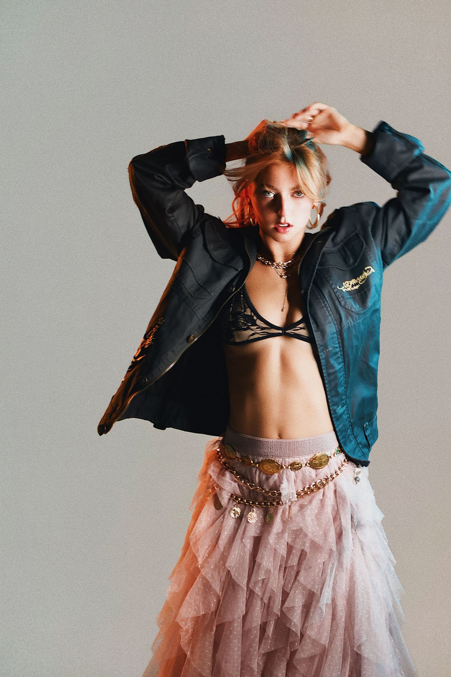 Fashion portrait with leather jacket and pink tulle skirt against gray studio backdrop.