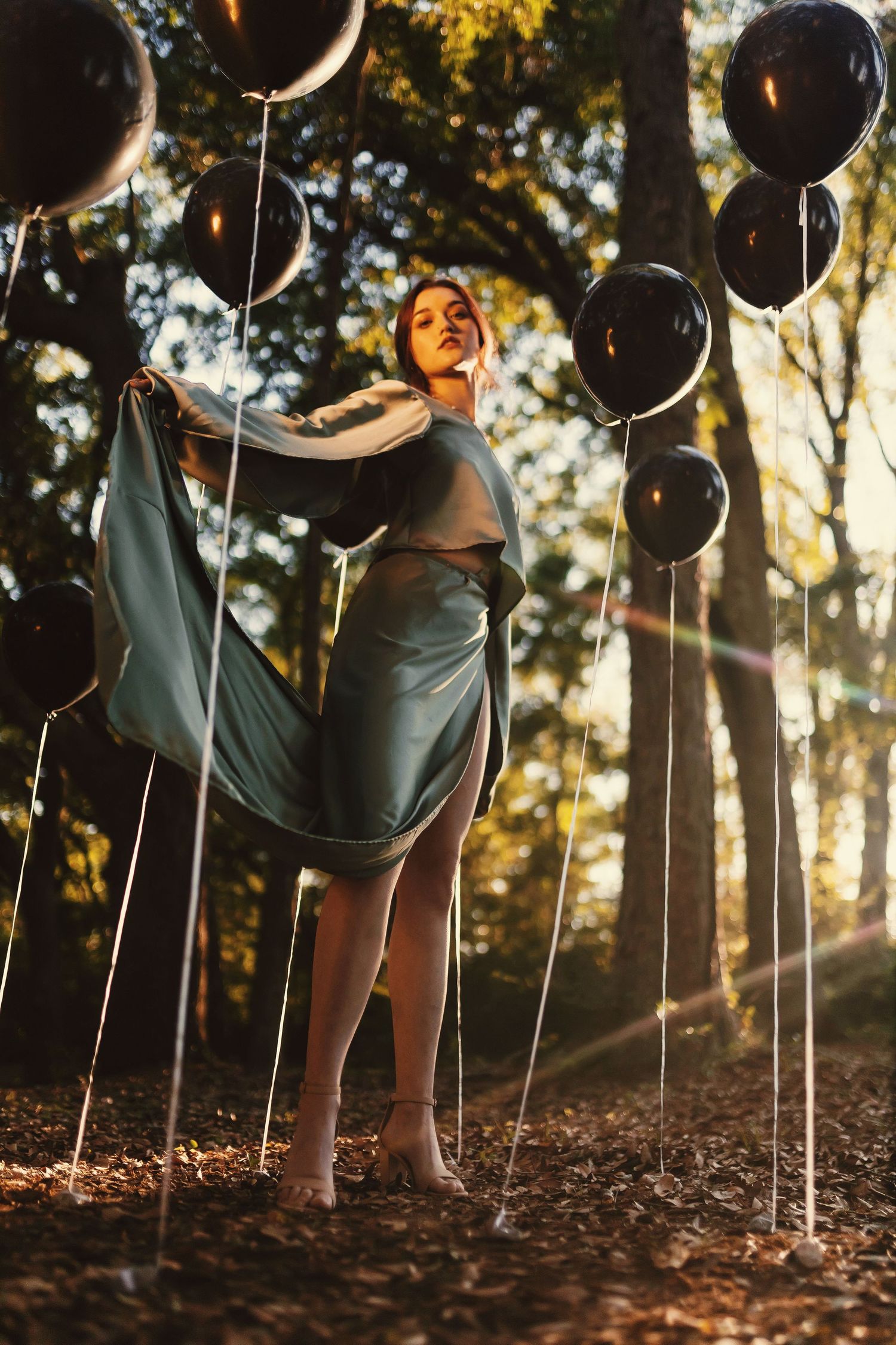 Artistic series of black balloons floating above autumn leaves on forest ground during golden hour lighting.