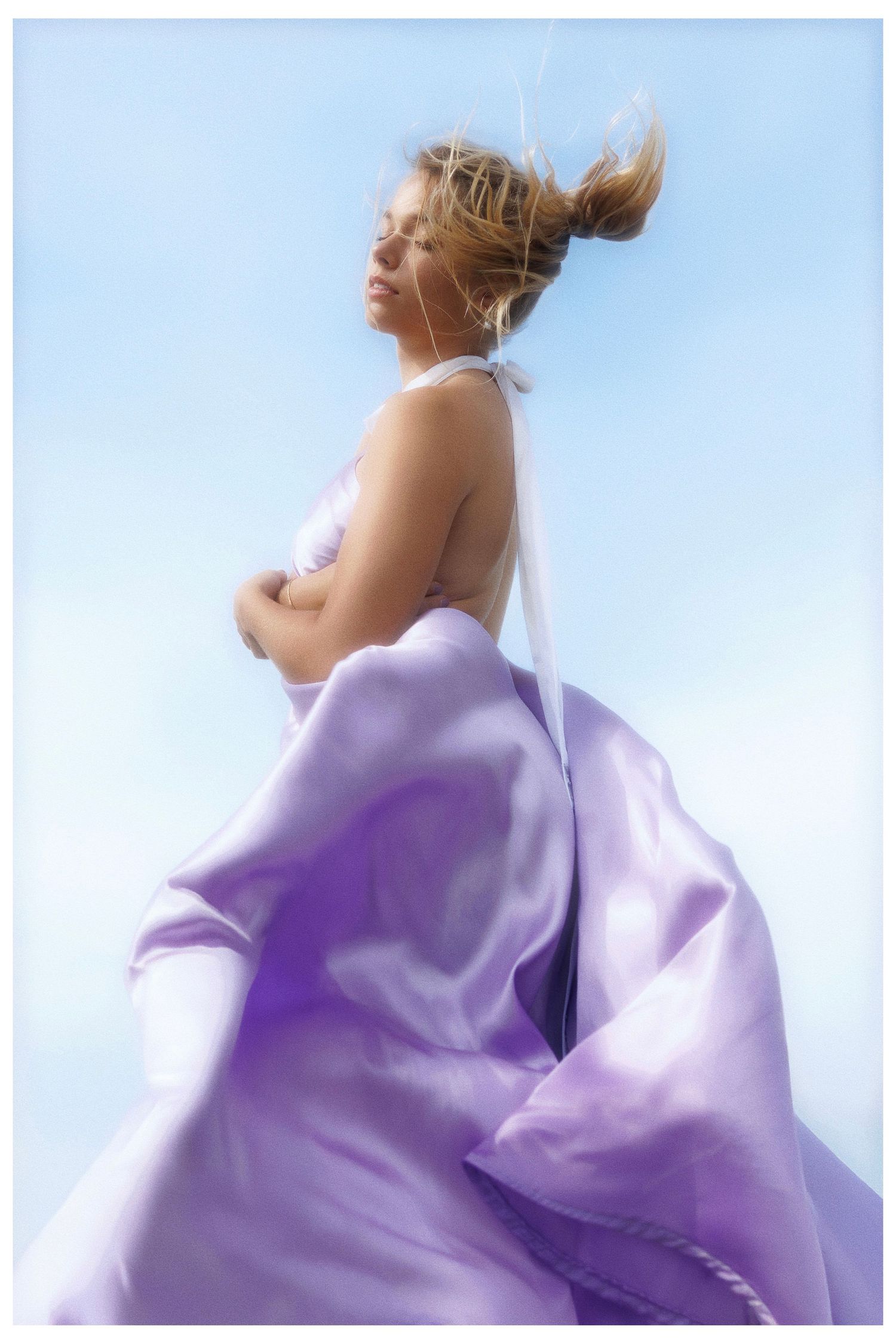 Ethereal fashion photo featuring flowing purple fabric against blue sky with soft dreamy effect and movement.