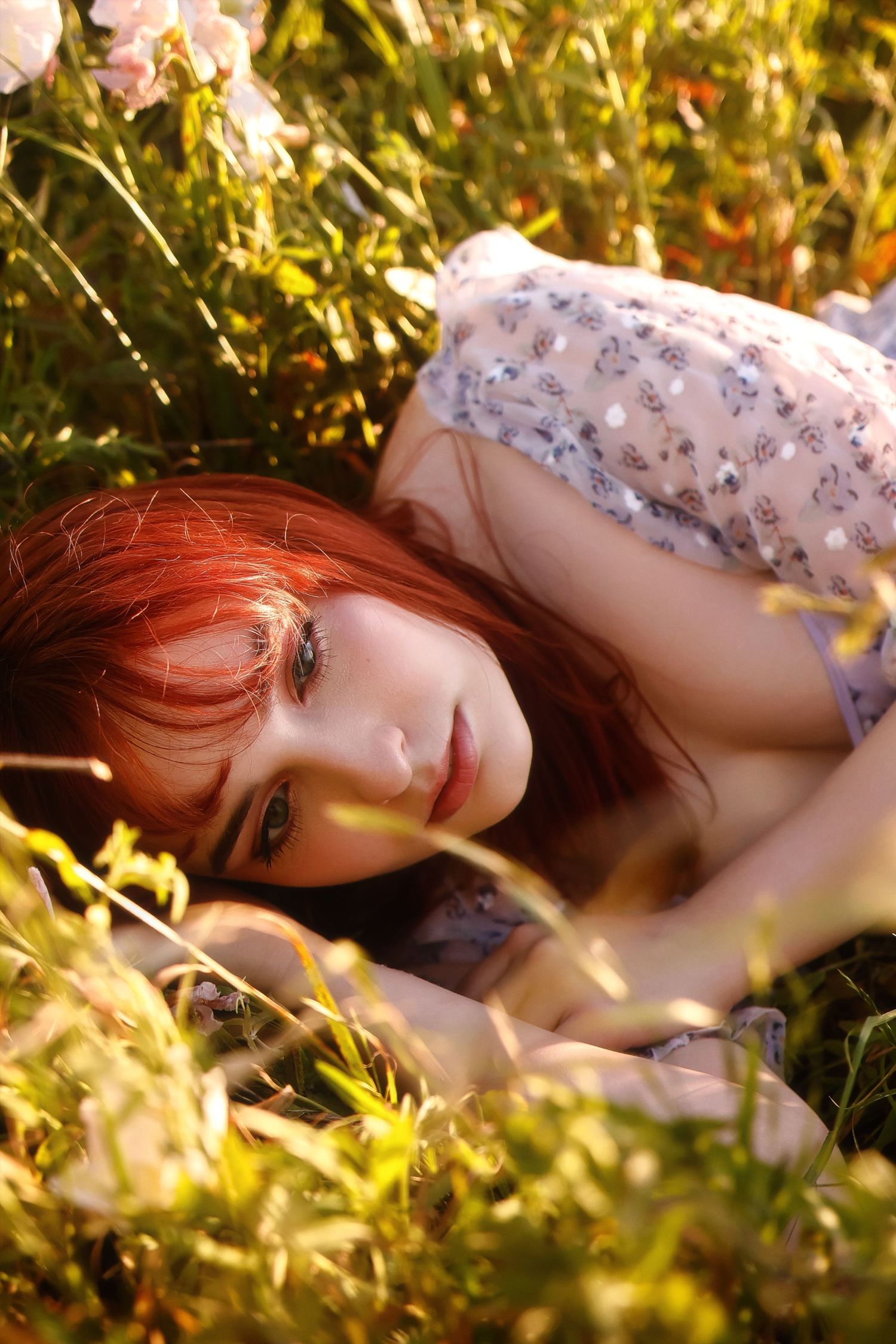 A person lying in soft grass with sunlight filtering through leaves creating a dreamy natural setting.