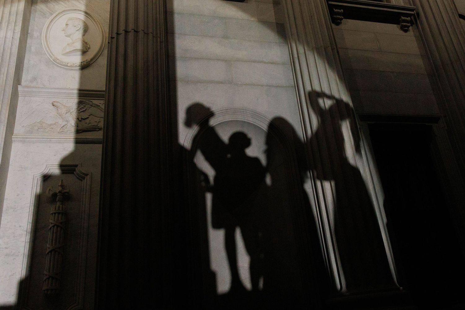 Black and white silhouette of figures projected on a wall, creating a dramatic shadow against a light background.