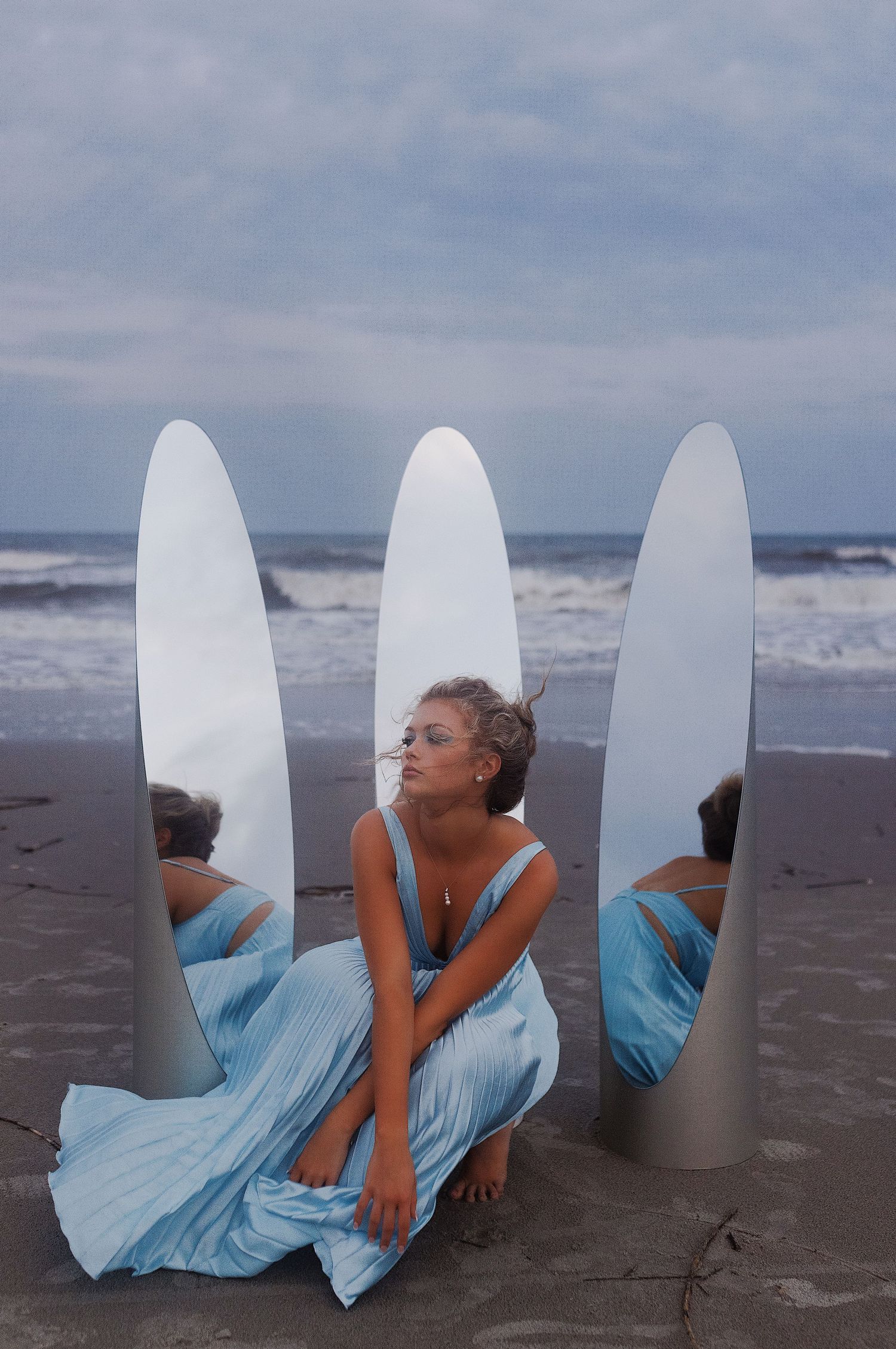 A person in a flowing light blue dress poses artistically on a beach with surfboards in a creative photo sequence.