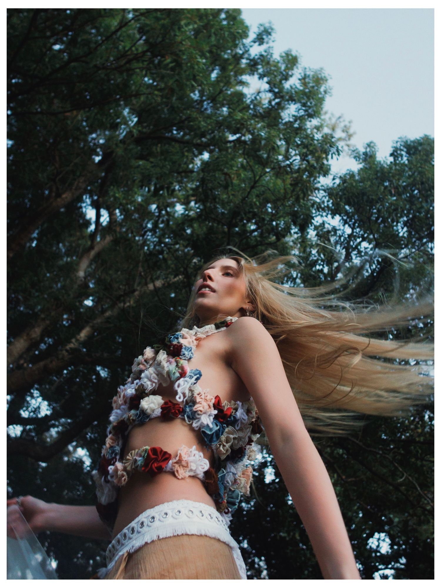 Artistic sequence of blonde hair flowing in the wind with floral crown against a backdrop of green trees.