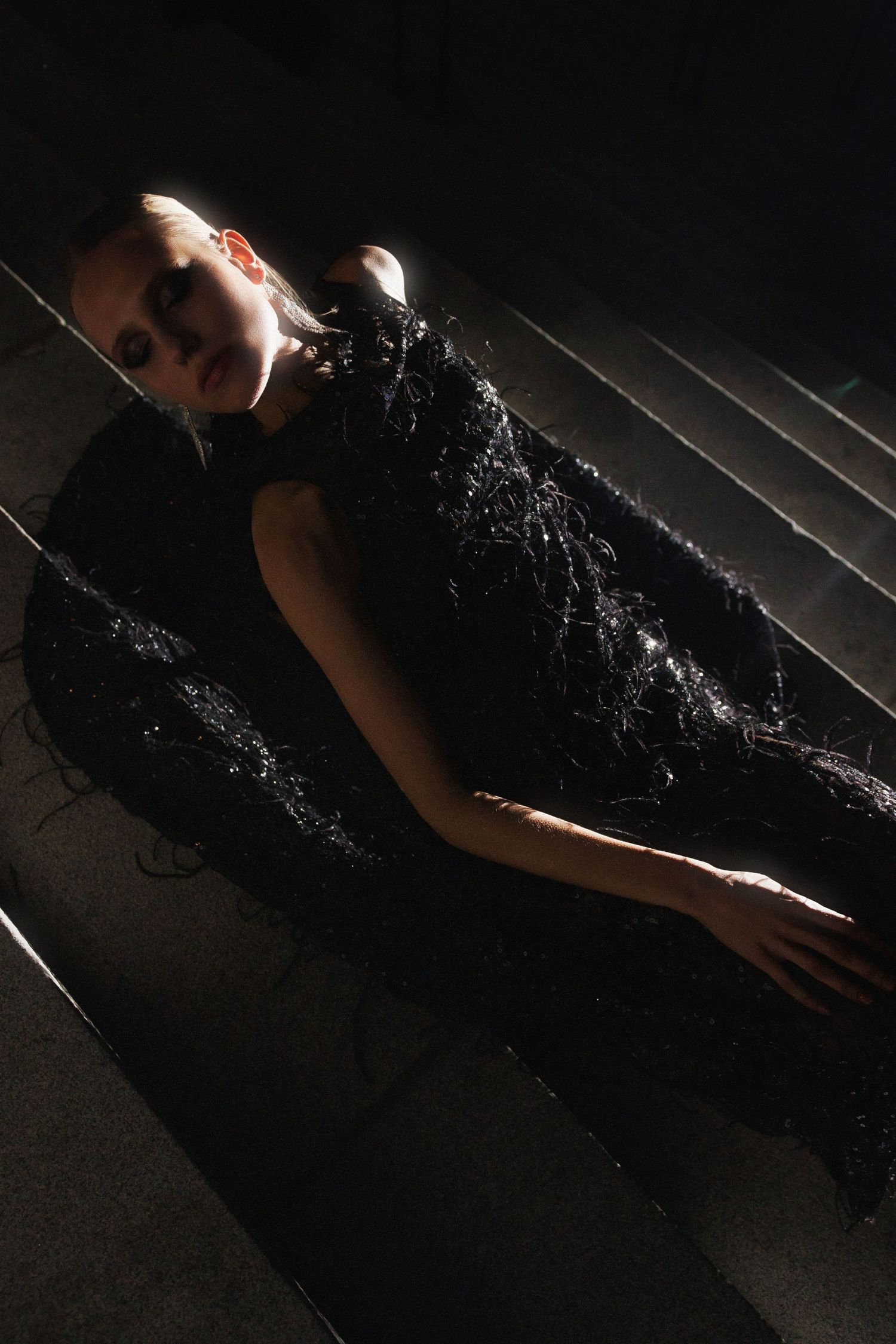 A long black lace evening gown lying elegantly on hardwood flooring in dramatic lighting.