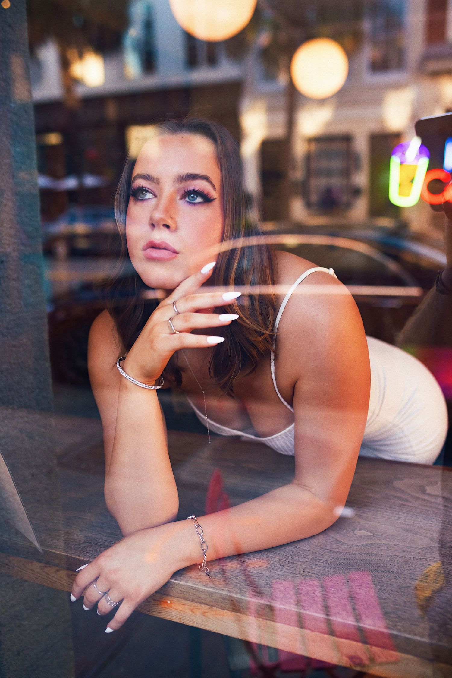 A person rests their head on their hand while gazing through a window in a dimly lit cafe setting.