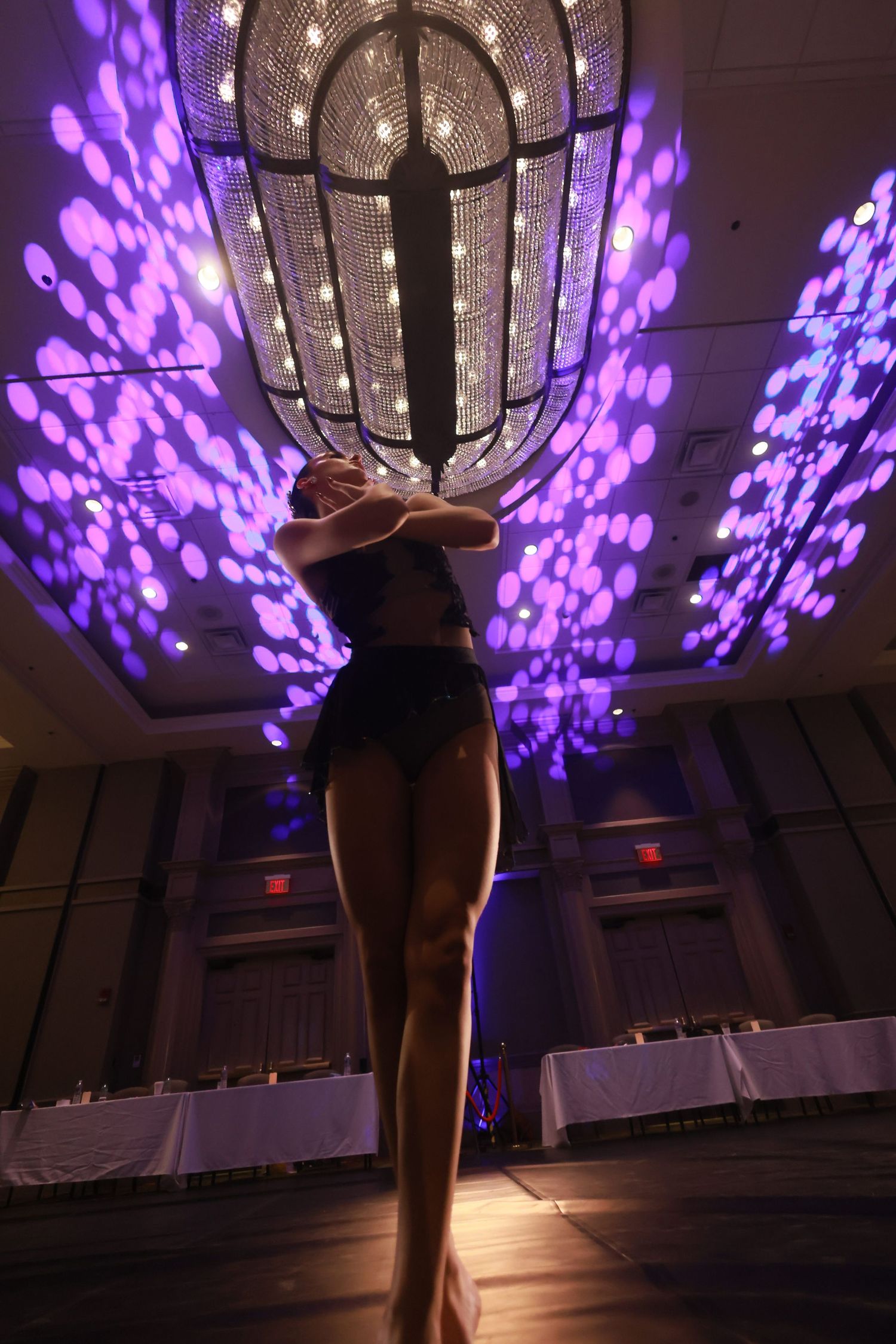 A dancer silhouetted against dramatic purple lighting and a grand chandelier in an elegant ballroom setting.