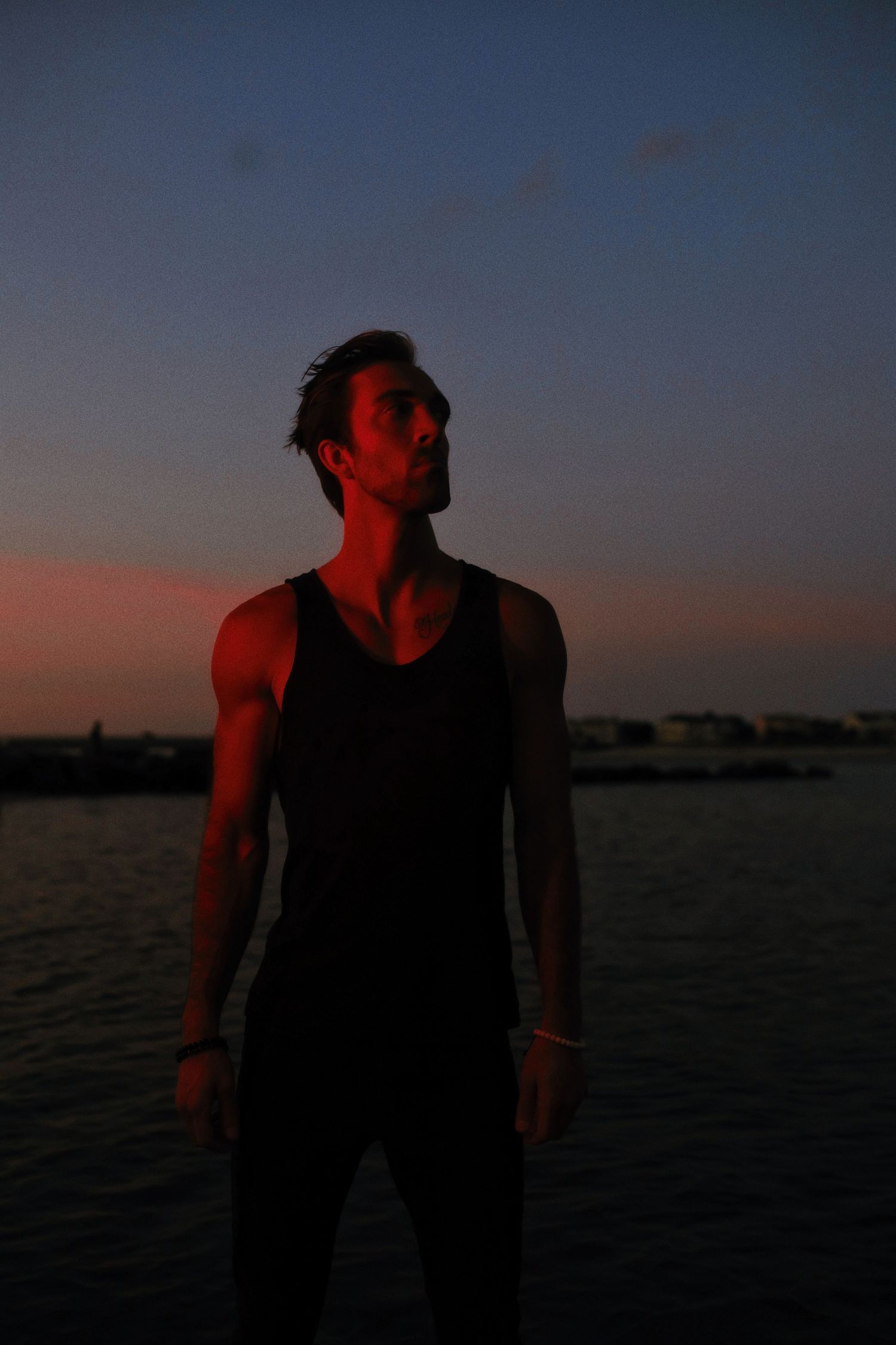 Silhouetted figure stands against a dramatic sunset over calm waters, cast in deep red and orange hues.