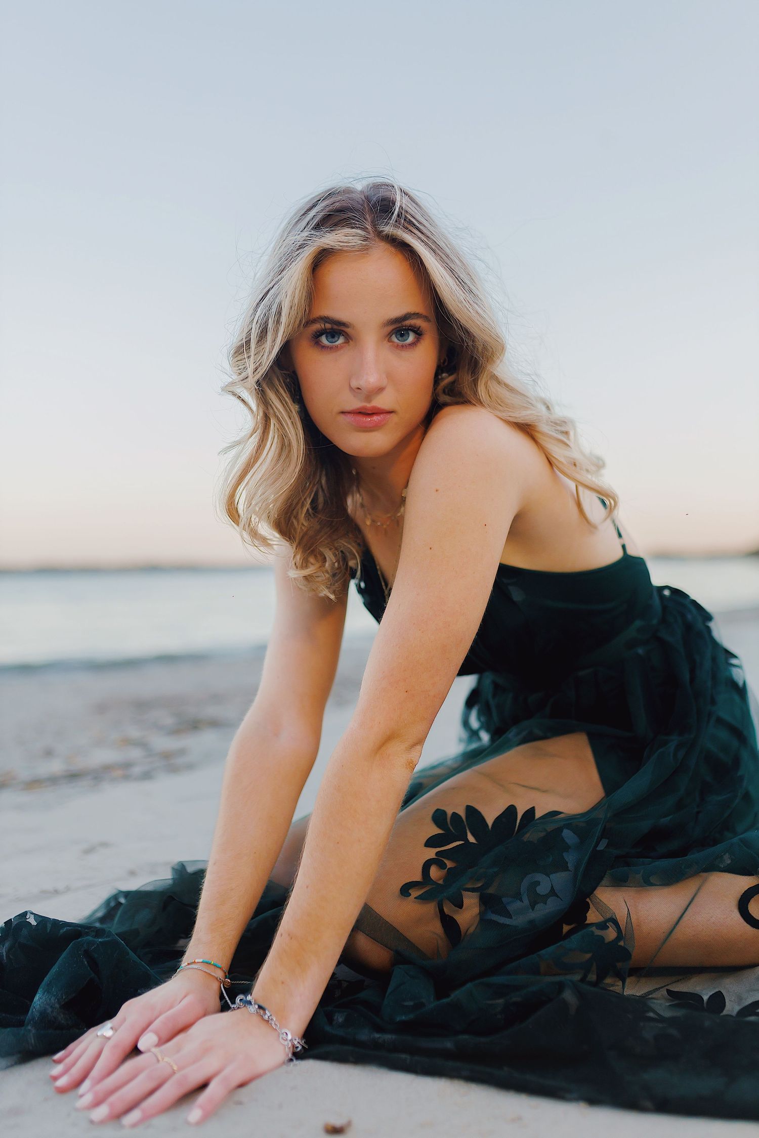A person in a black dress poses elegantly on a sandy beach during sunset creating a dreamy coastal photoshoot.