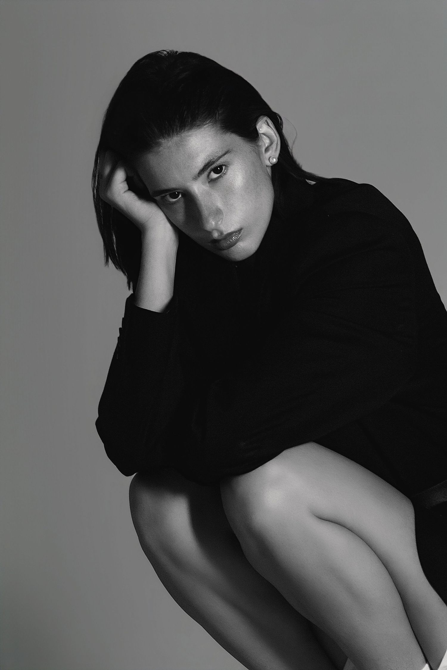 Black and white fashion portrait of model in turtleneck sweater posing against gray background in minimalist style.