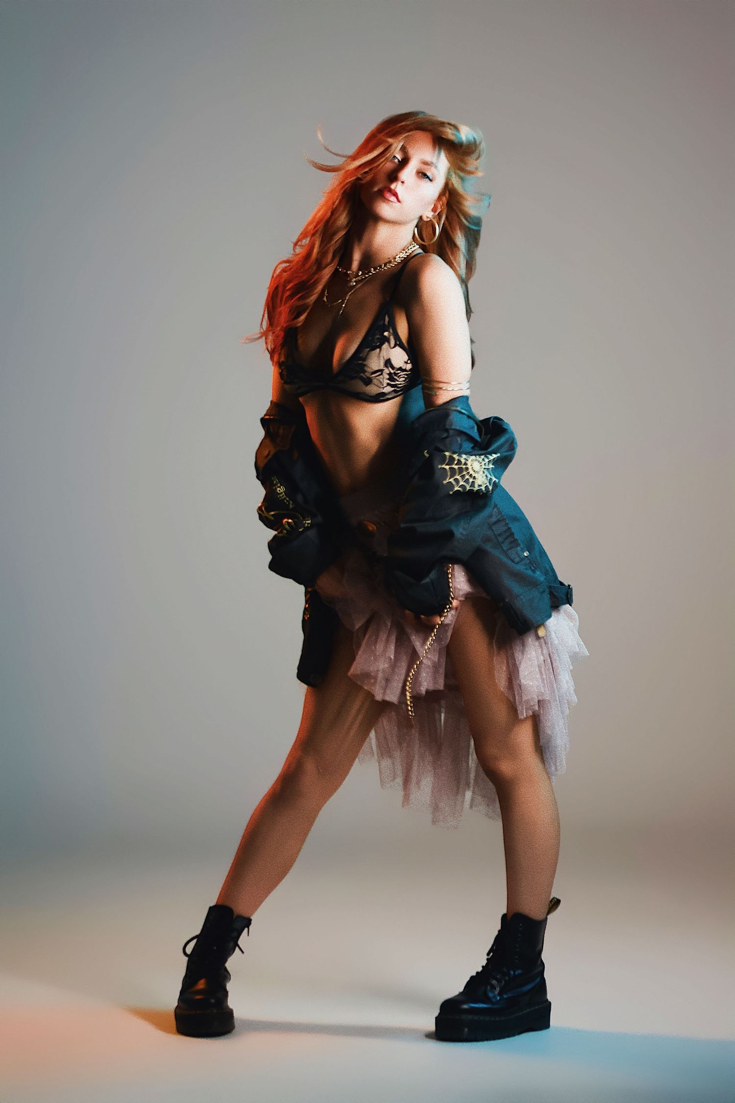 Stylish fashion portrait of model with flowing red hair wearing black top, tulle skirt and combat boots in studio setting.