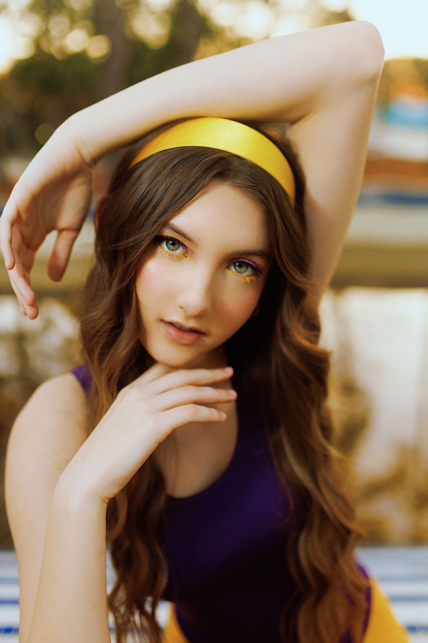 Portrait of a woman with long brown hair wearing a yellow headband and purple top in warm outdoor lighting.