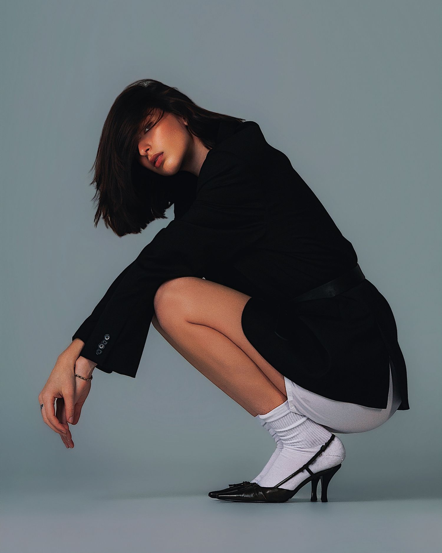 Figure in black clothing and white socks strikes dynamic dance poses against gray backdrop, creating artistic movement sequence.