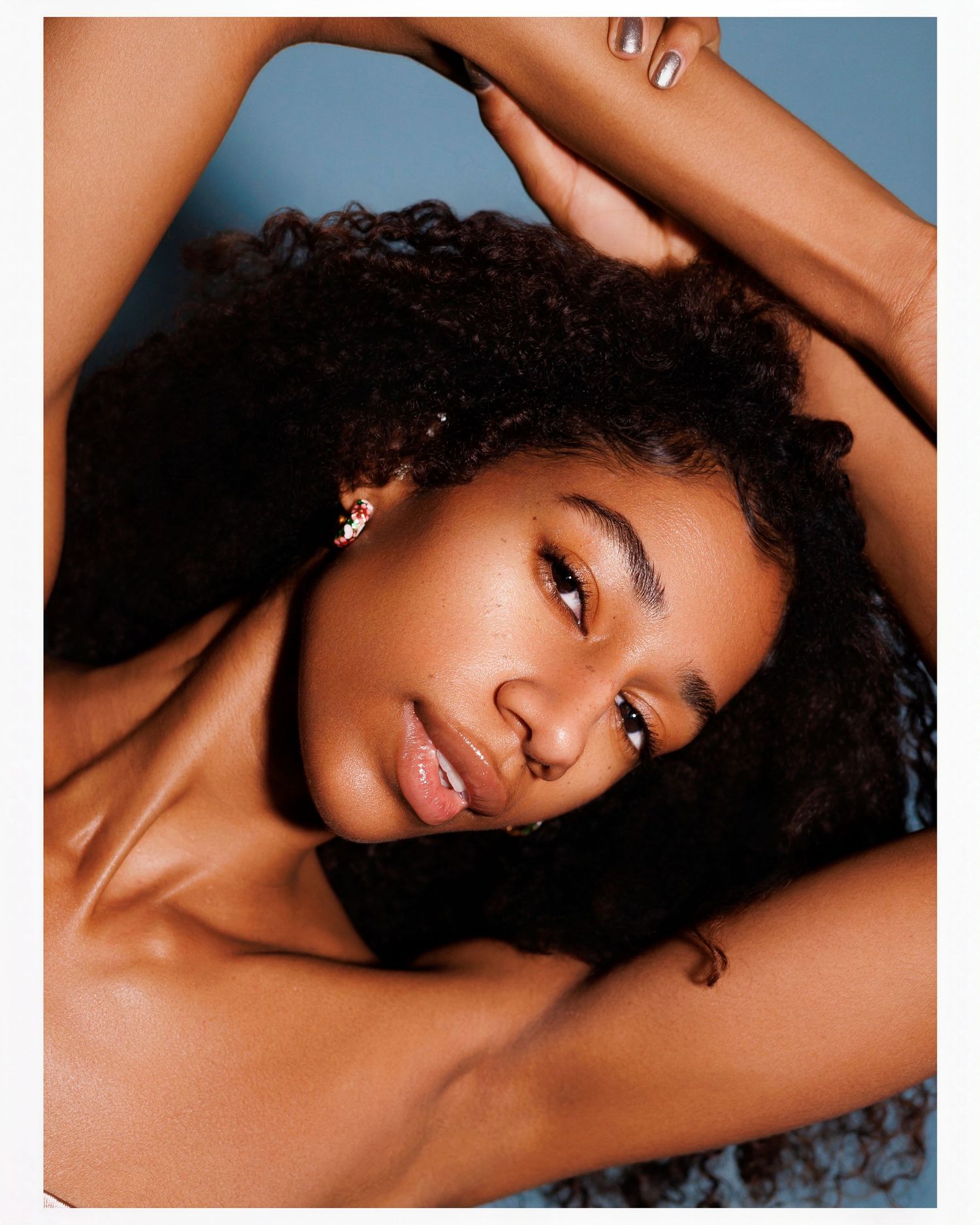 Artistic beauty portrait with natural curly hair against blue background showing glowing skin and elegant pose.