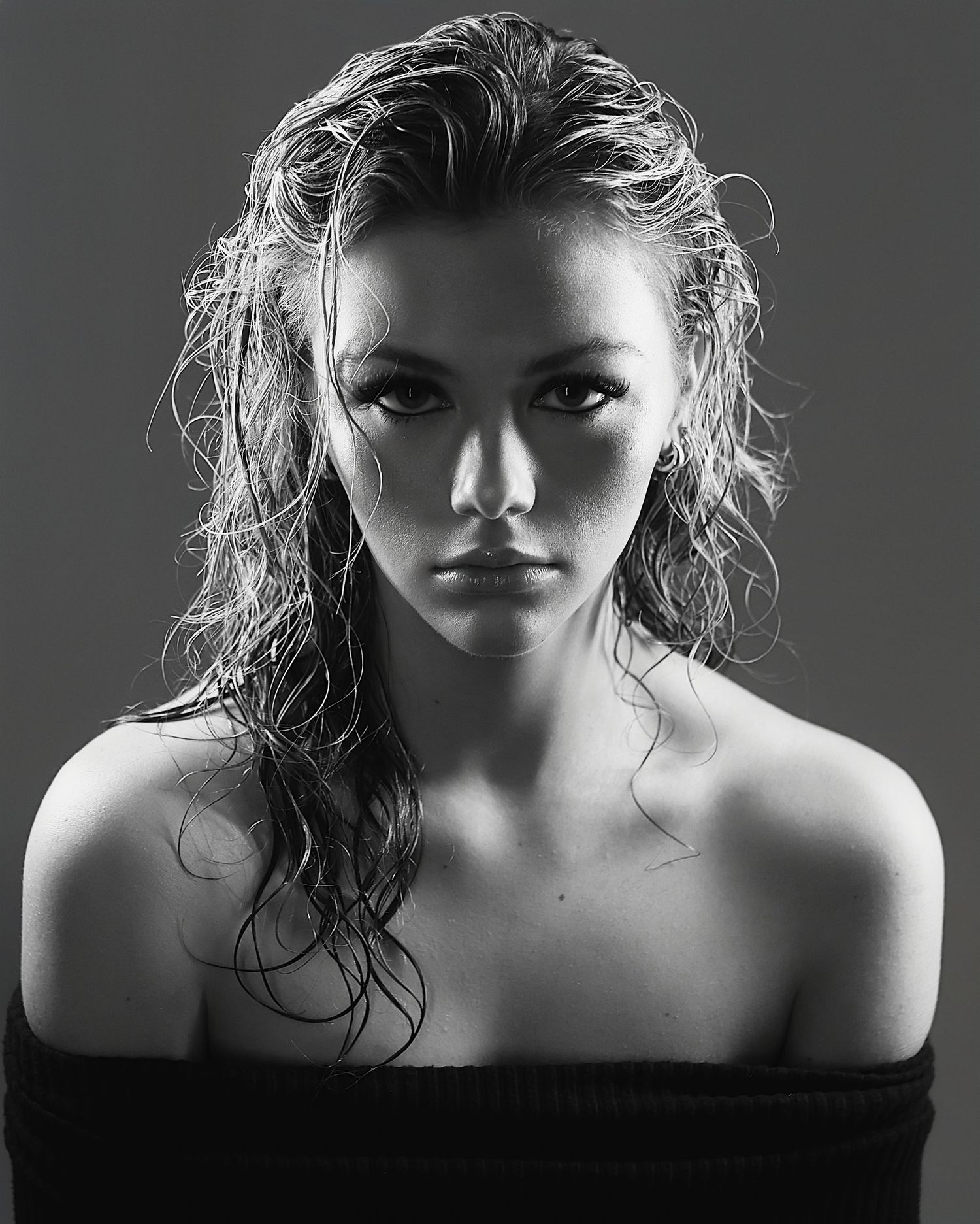 A dramatic black and white portrait showing a wet-haired figure with intense gaze against dark background.