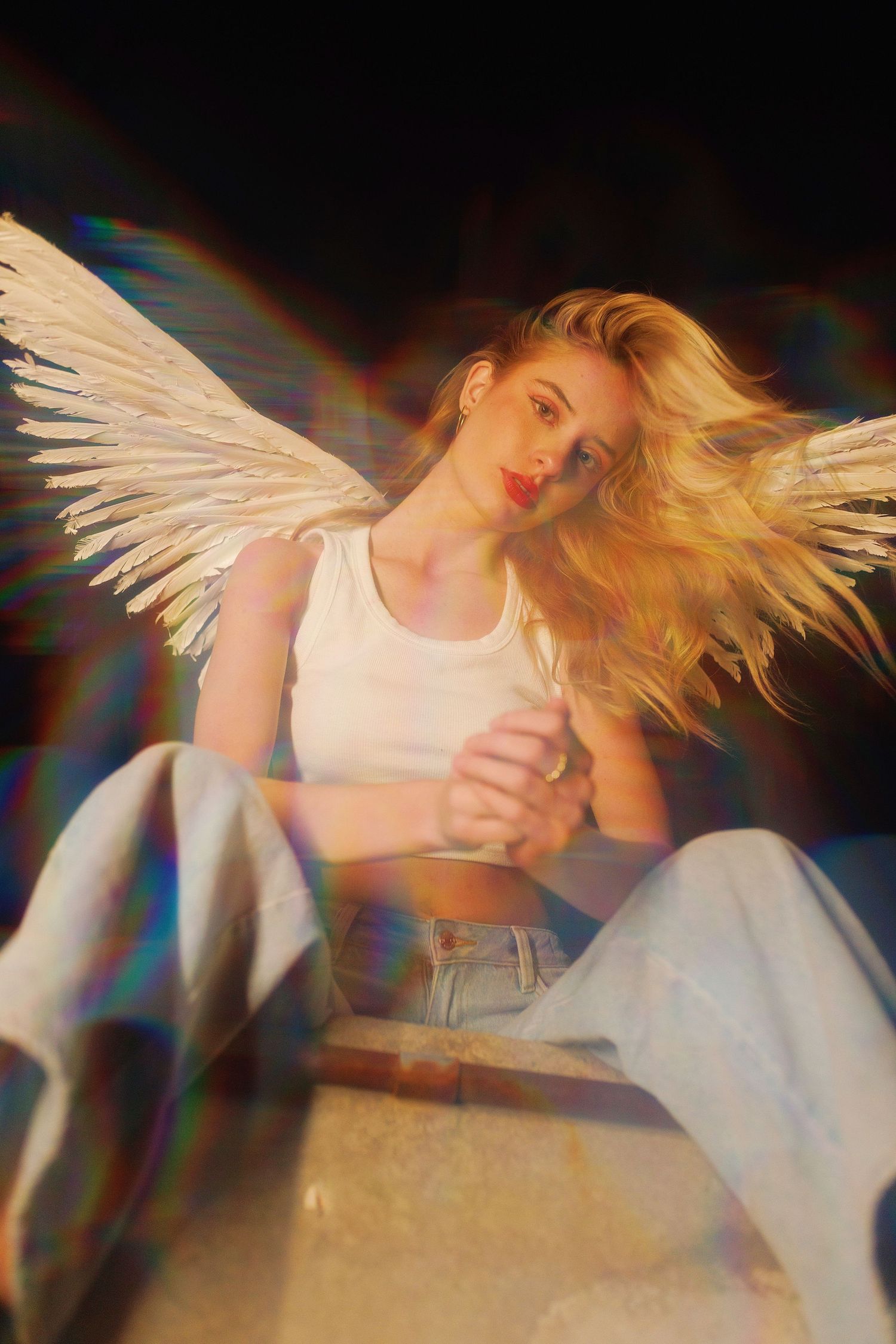 Artistic photo of a person with white angel wings wearing casual white top and jeans with flowing blonde hair in motion.