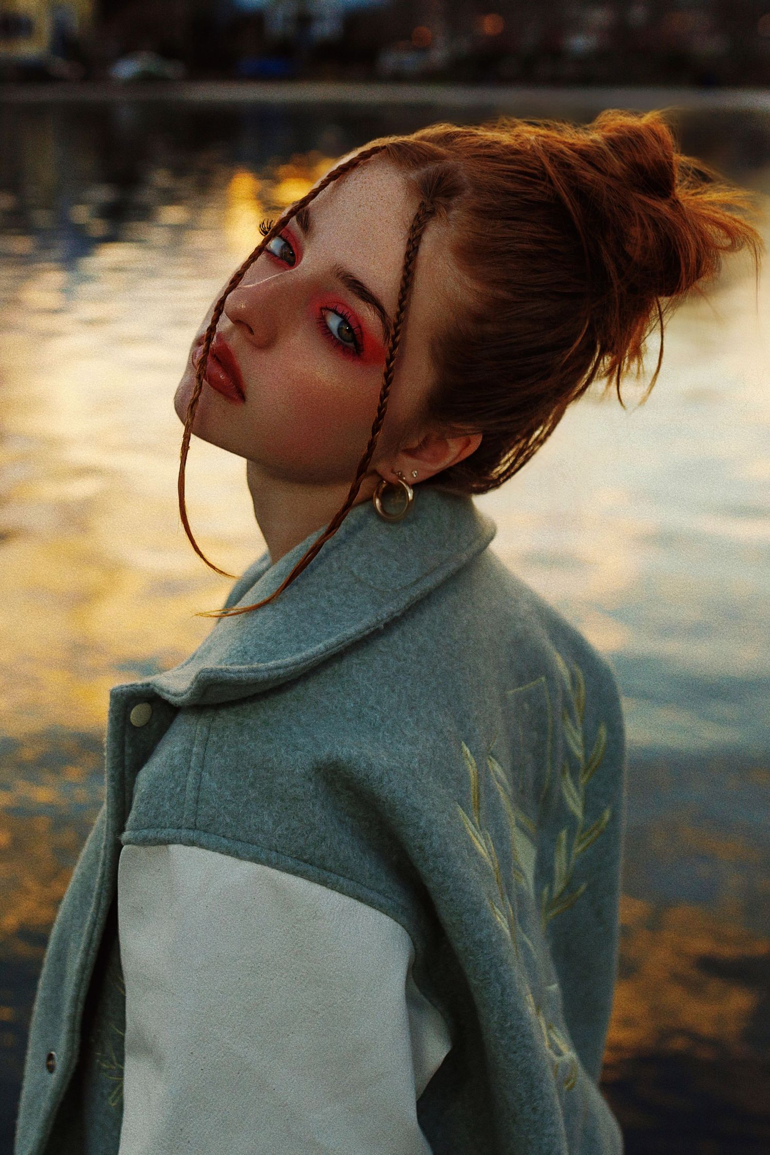 A stylized portrait at sunset featuring dramatic red eye makeup and a two-toned green and white jacket.