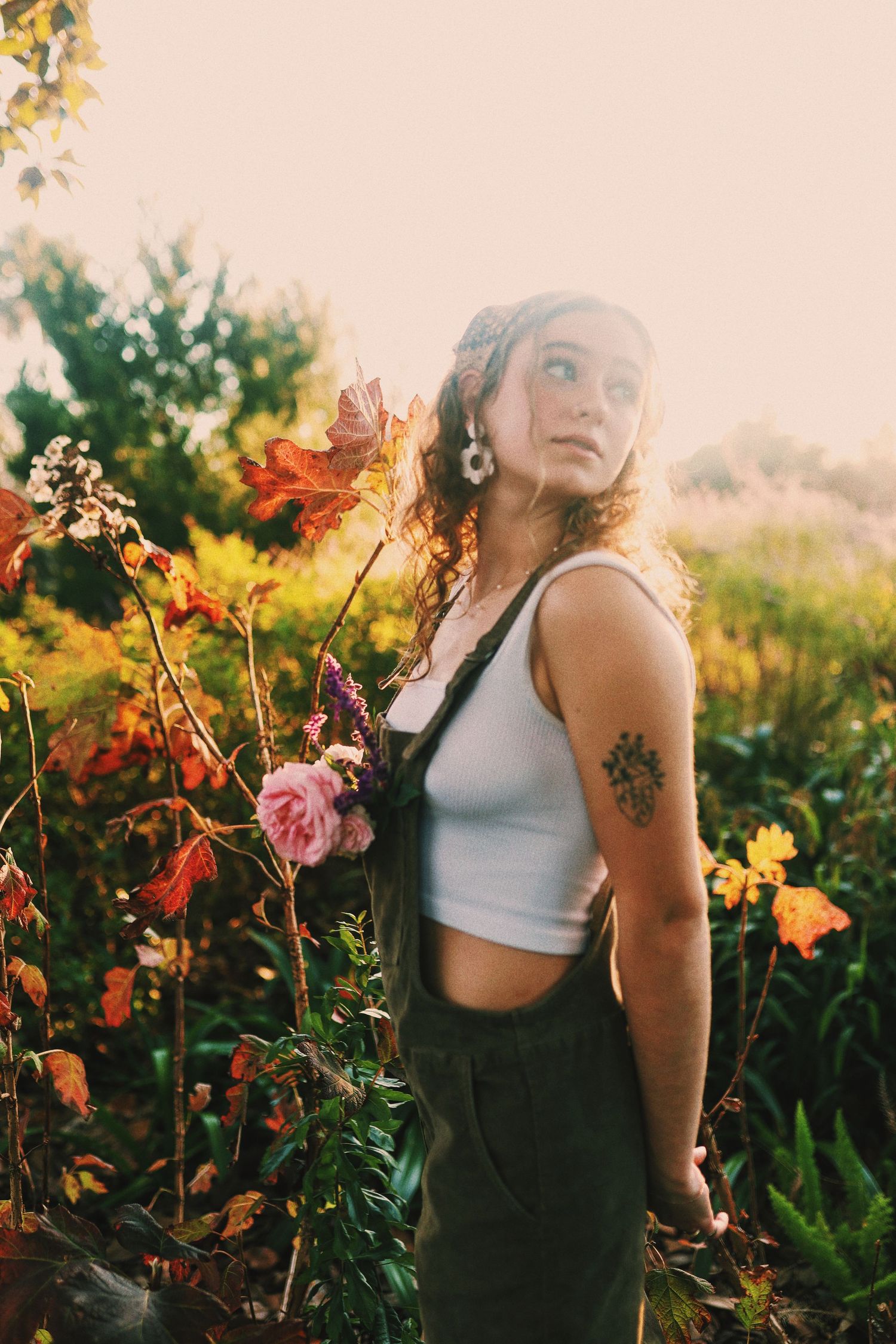 A figure stands in a vibrant garden at golden hour surrounded by colorful wildflowers and natural sunlight.