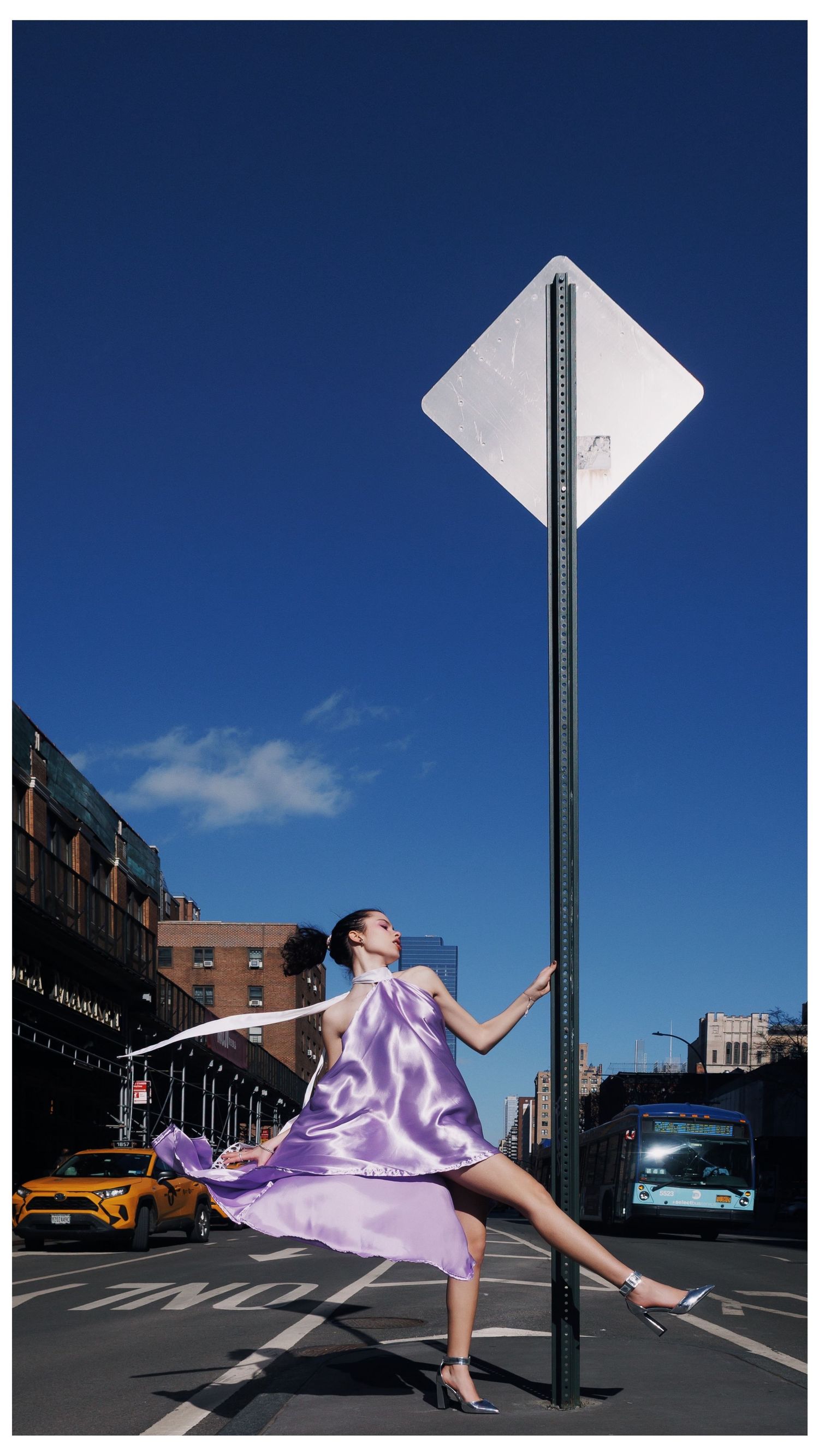 A dancer in flowing purple fabric performs graceful movements on an urban street corner against a deep blue sky.