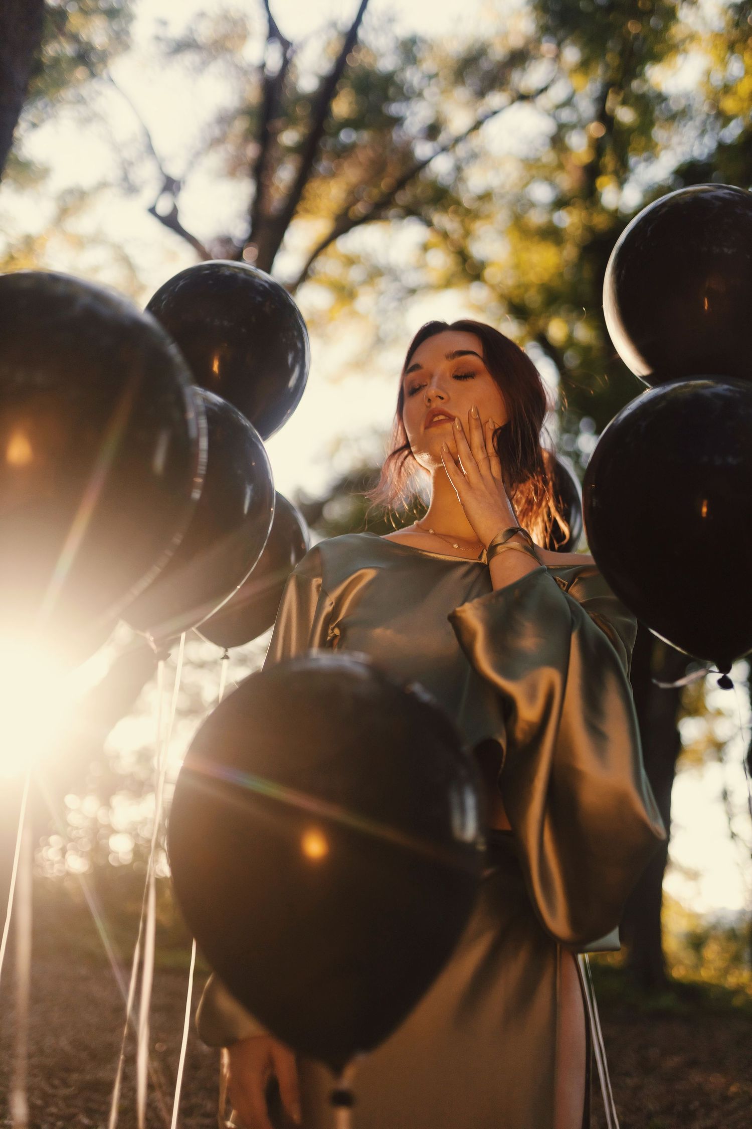 Atmospheric outdoor scene with black balloons and dramatic sunlight filtering through trees creating a magical autumn mood.