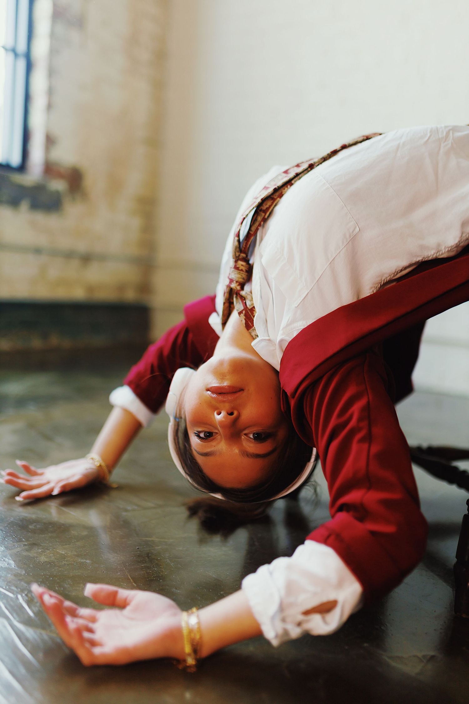 A person in a burgundy sweater leans backwards in a dramatic dance pose on a dark floor.