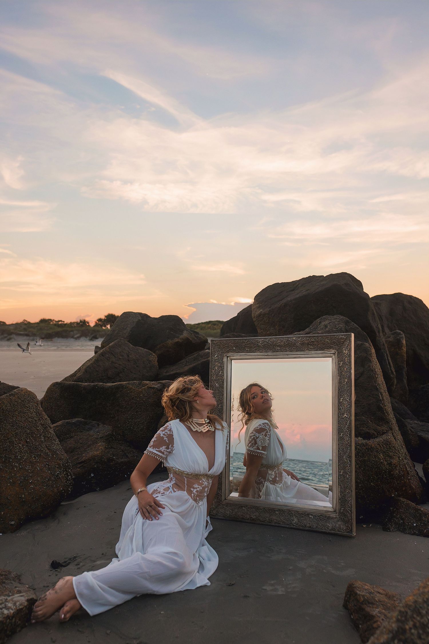 A creative sunset photoshoot with a mirror prop on rocky terrain capturing reflections and warm evening light.