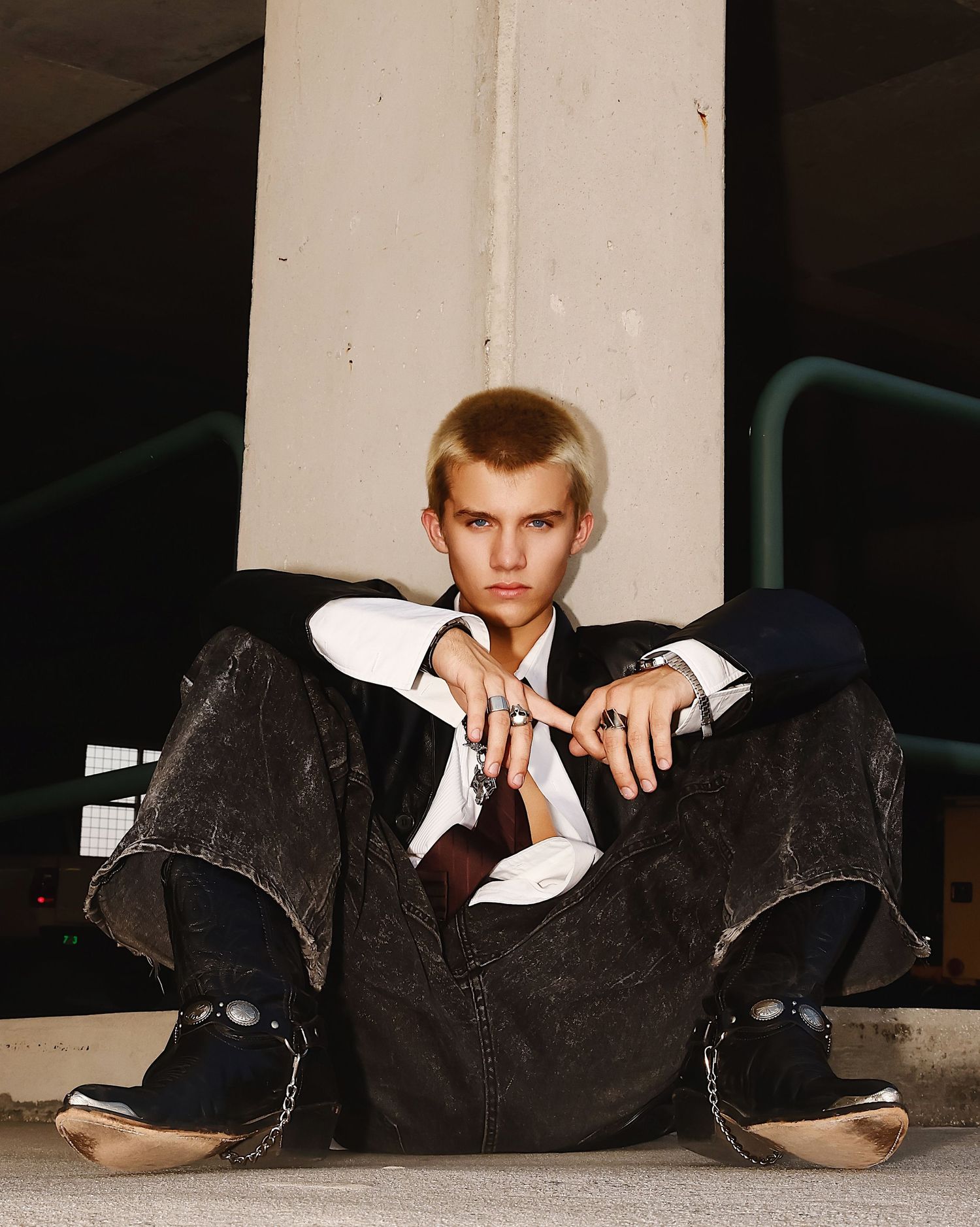 Young person in a suit sits on the ground in a casual pose against a white column.