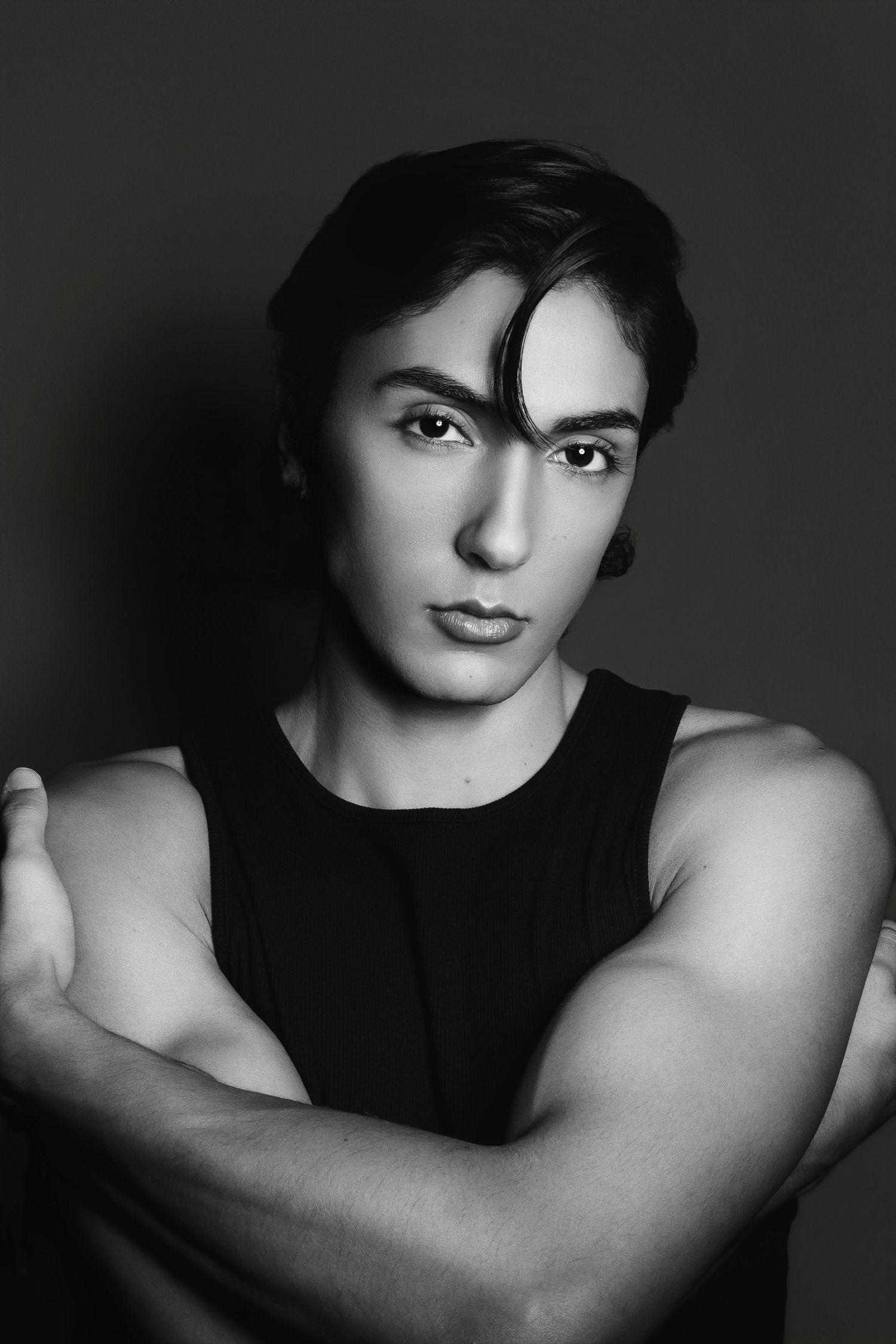 Black and white portrait featuring a striking composition with dramatic lighting and confident pose in dark sleeveless attire.