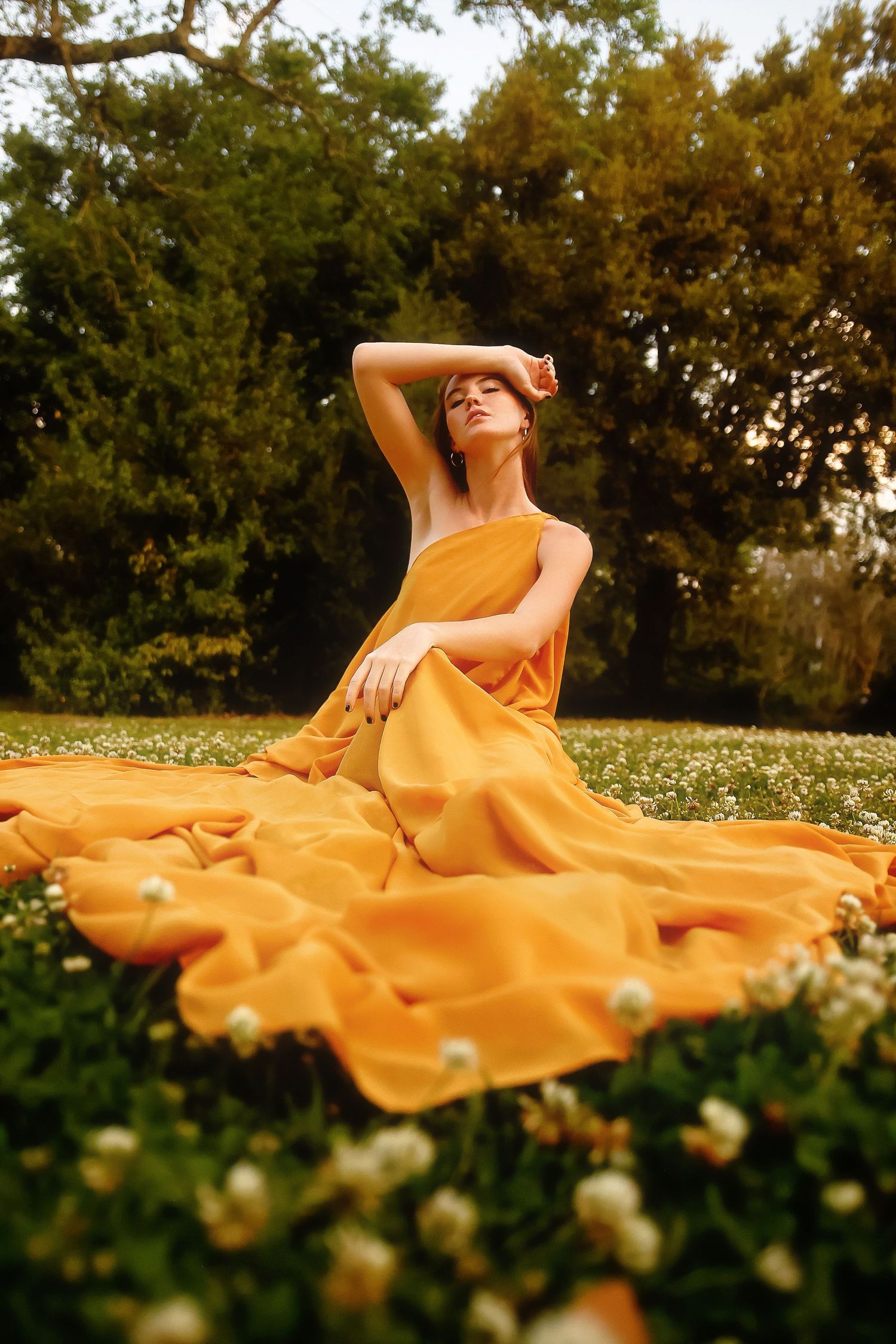 Flowing yellow dress spreads across a meadow of white wildflowers during golden hour at sunset.