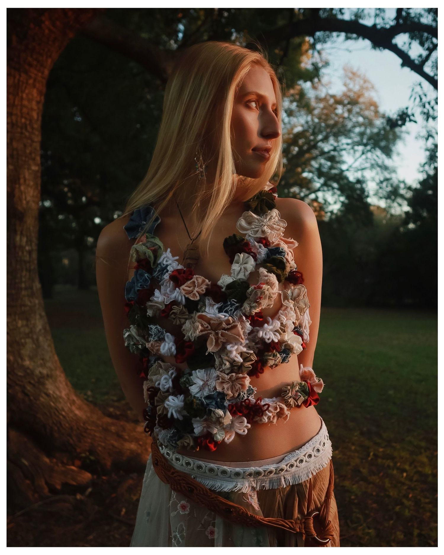 Person in white dress poses with white and pink flowers against sunset backdrop in moody autumn outdoor setting.