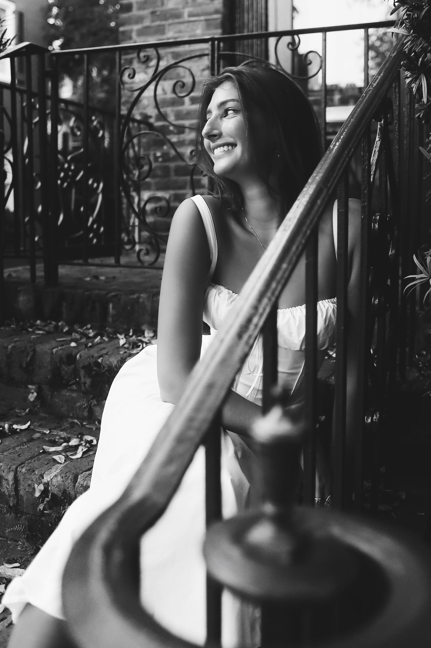 A black and white photo series showing someone sitting by ornate iron railings while laughing joyfully.