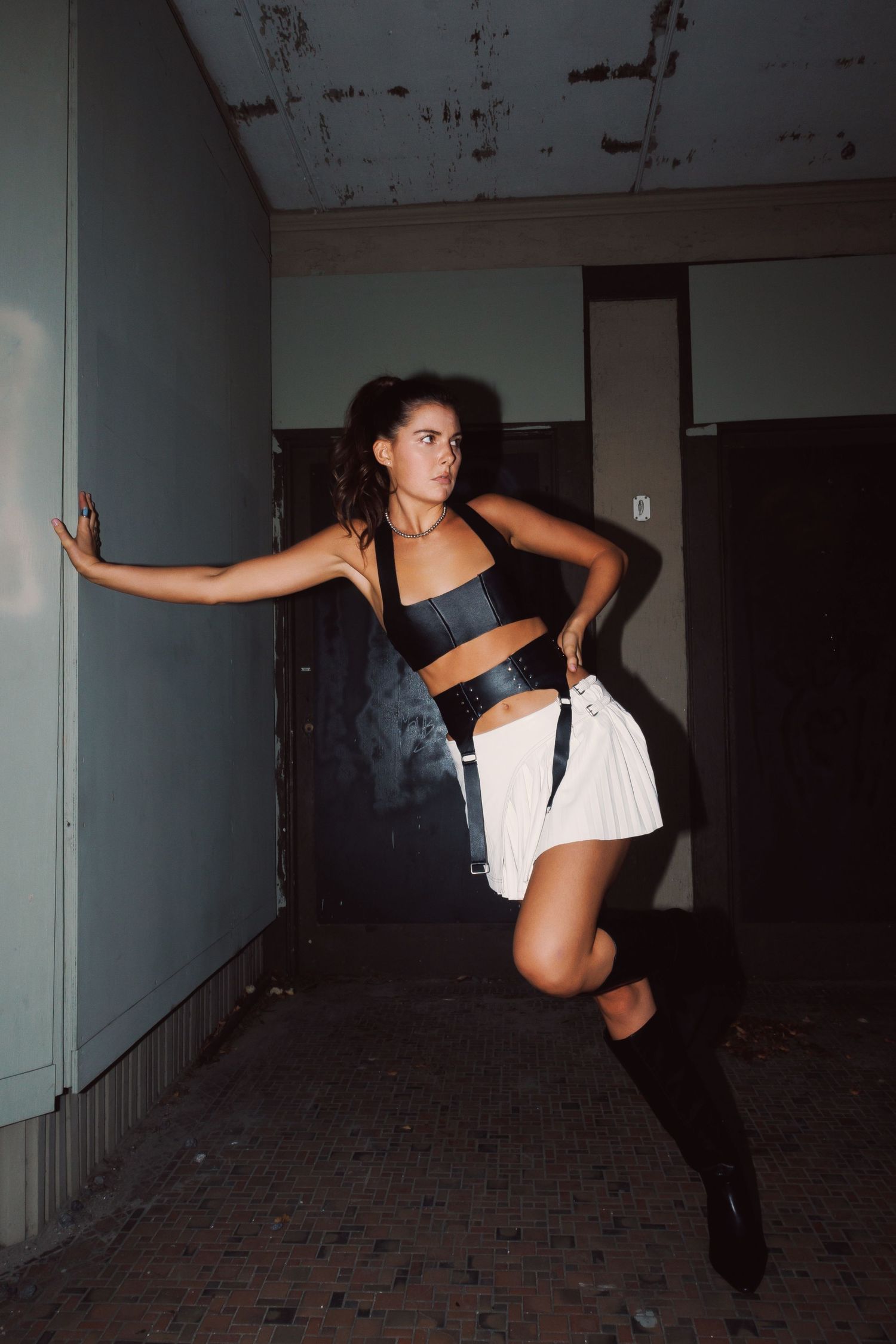 A dancer performs dynamic movements in a dark, abandoned hallway wearing black and white attire.